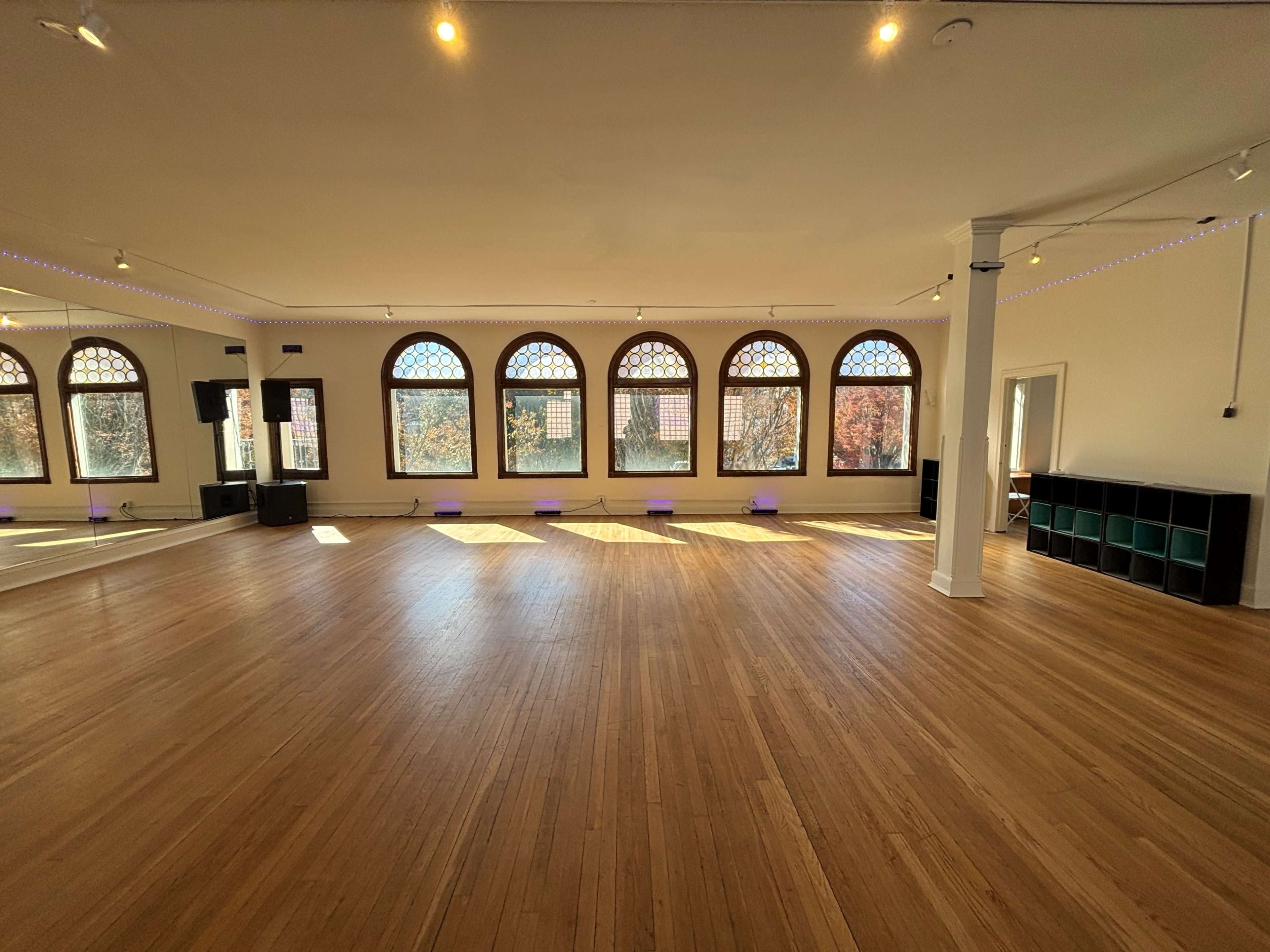 A spacious, well-lit studio features hardwood floors and large arched windows, with audio equipment positioned in one corner.