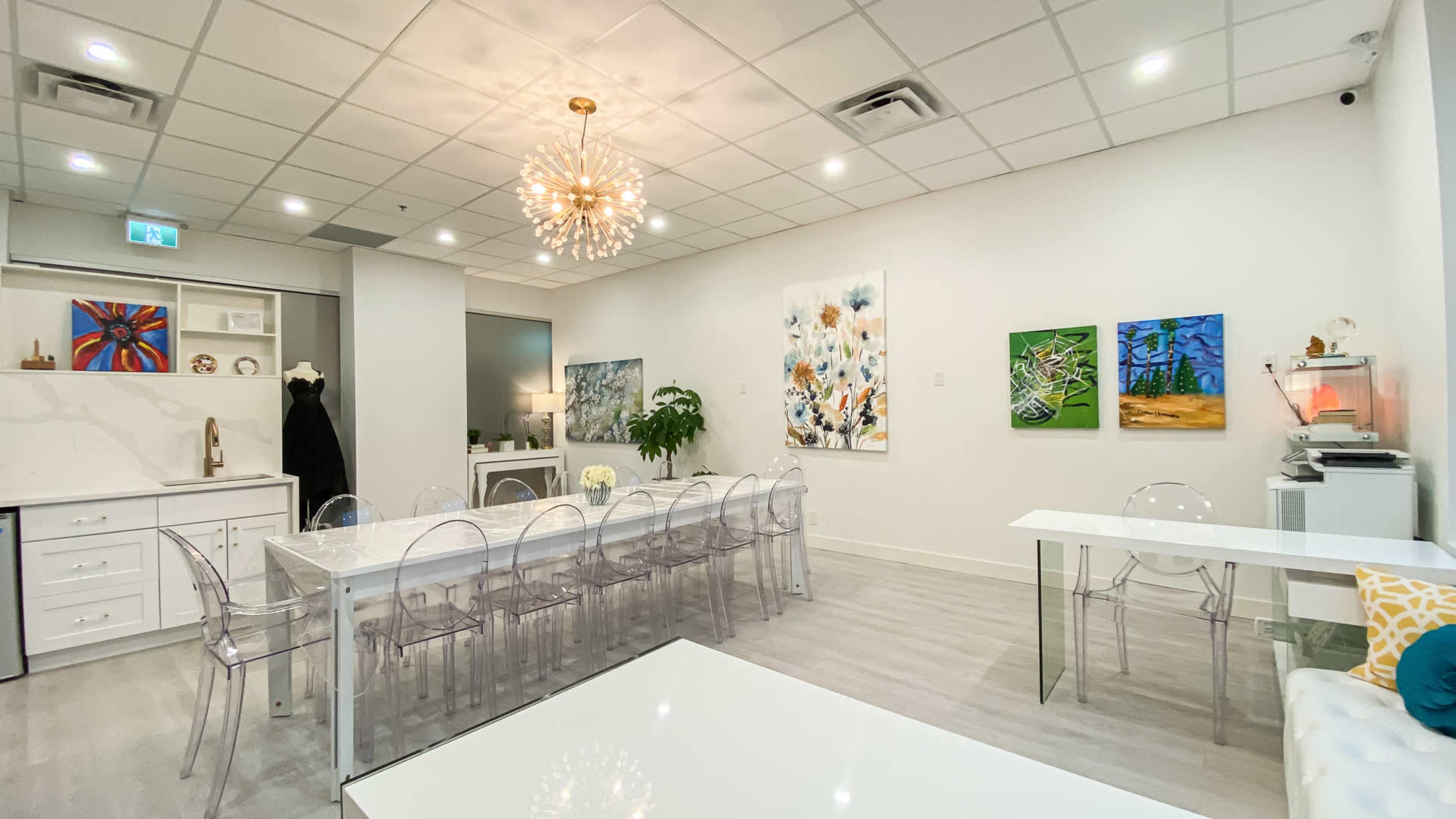 A modern meeting room with a long transparent table, acrylic chairs, and colorful artwork on the walls.