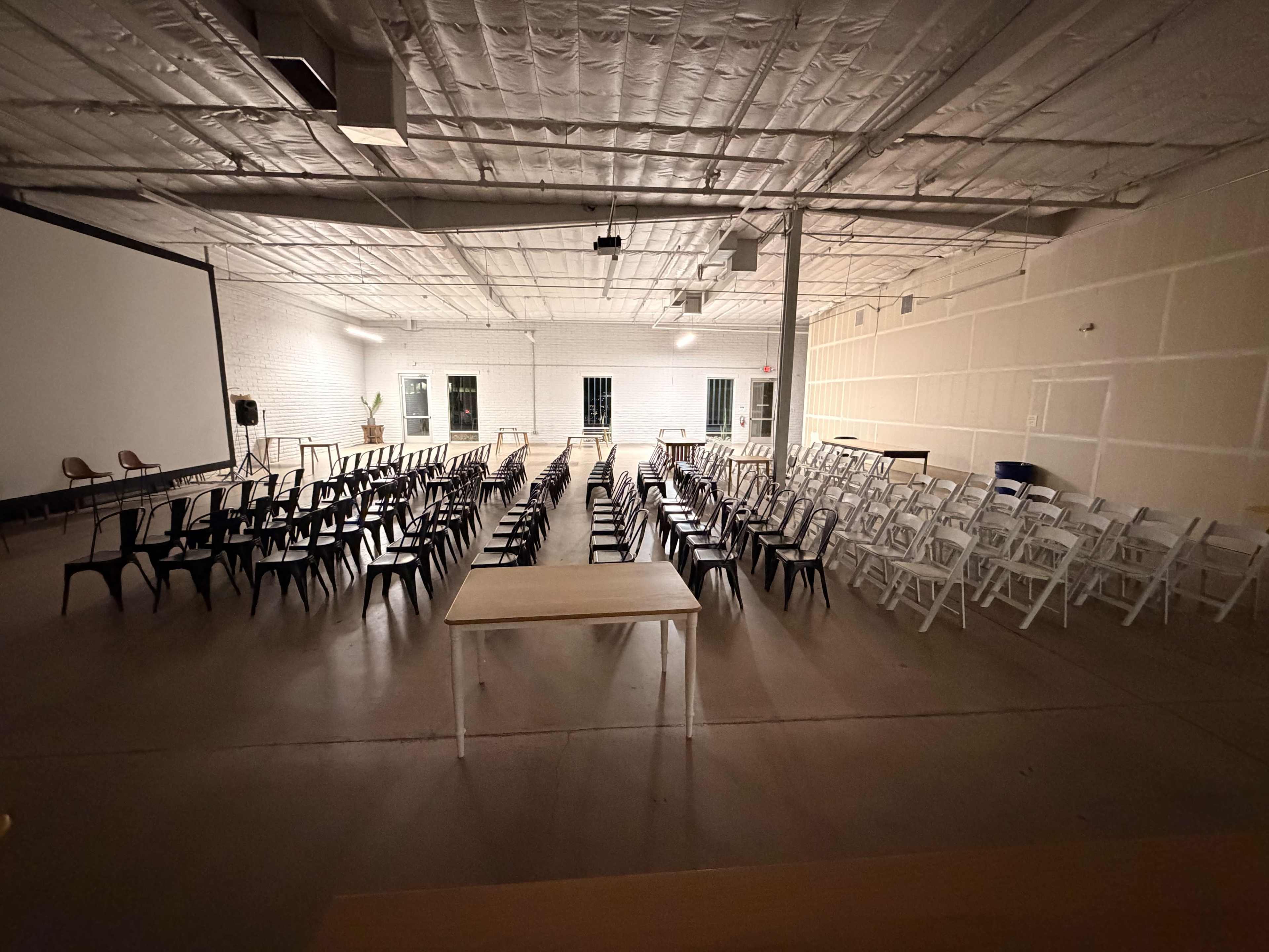 The image shows a spacious, empty room set up with rows of chairs facing a large projection screen.