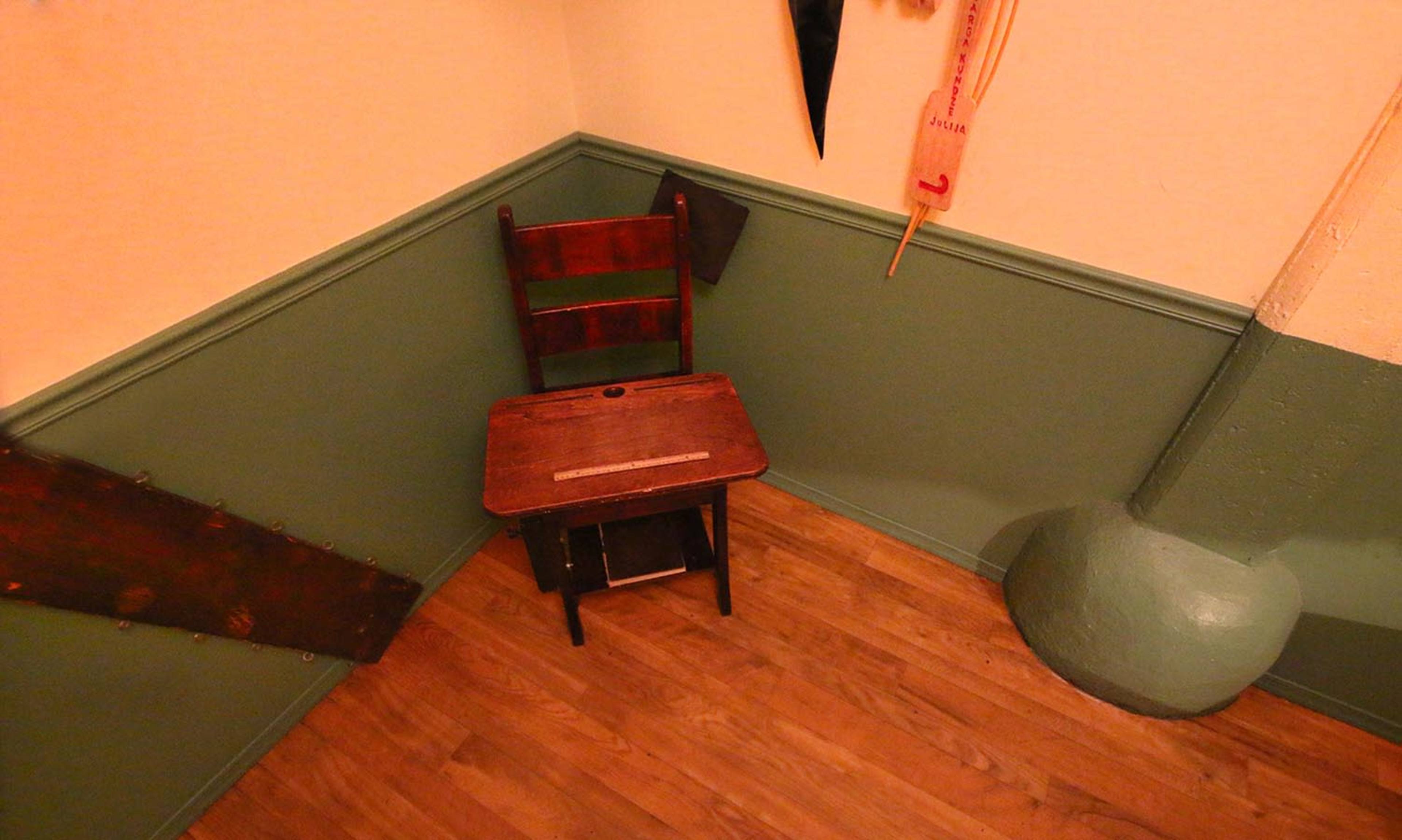 A wooden chair is positioned in the corner of a room with green-painted walls and a wooden floor.