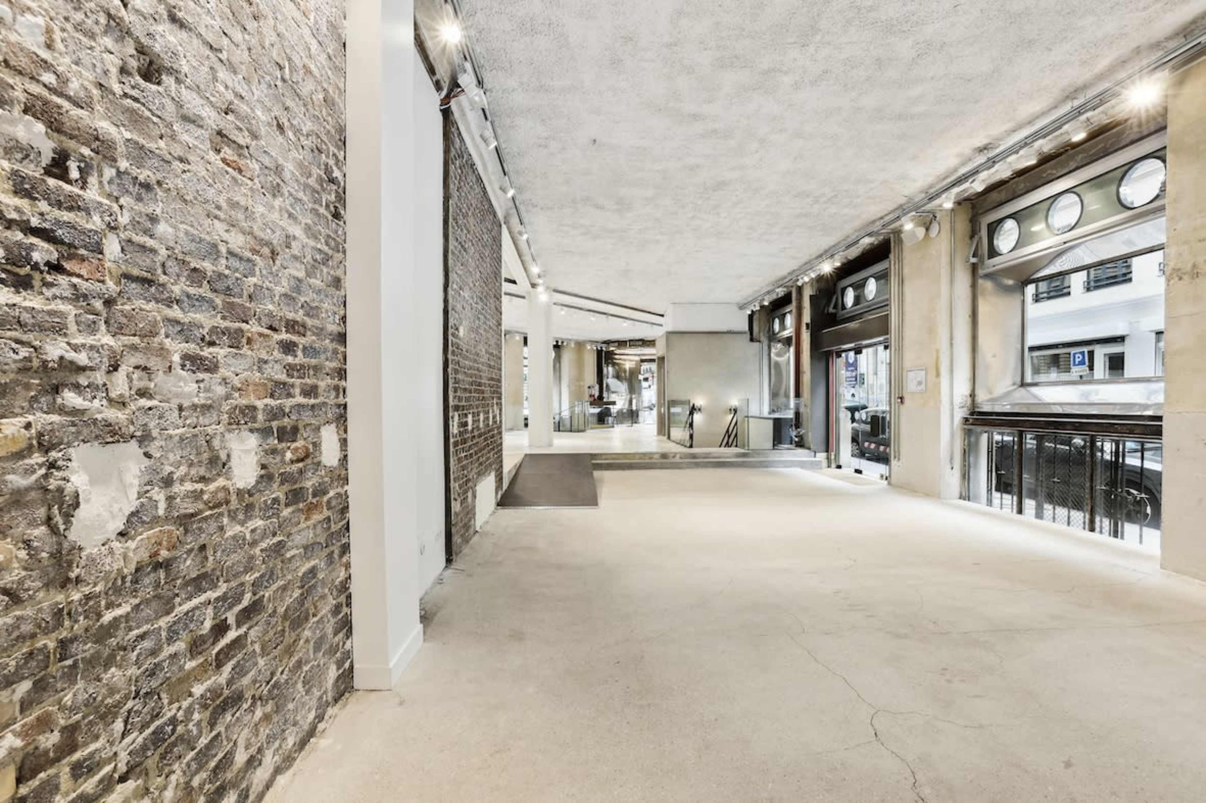 The image shows a spacious, modern interior with exposed brick walls and large windows.