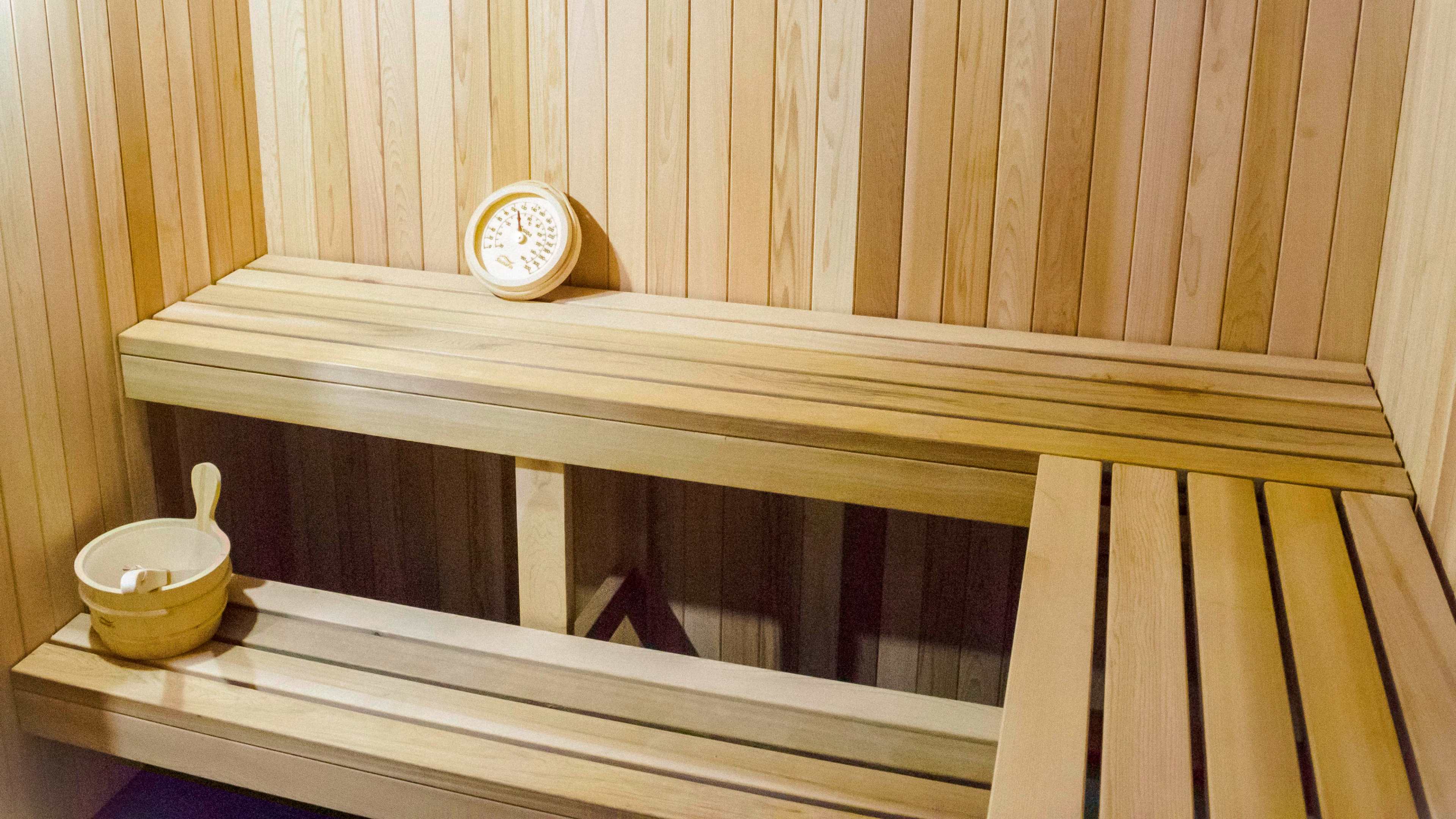 A wooden sauna interior with benches and a circular thermometer on the wall.