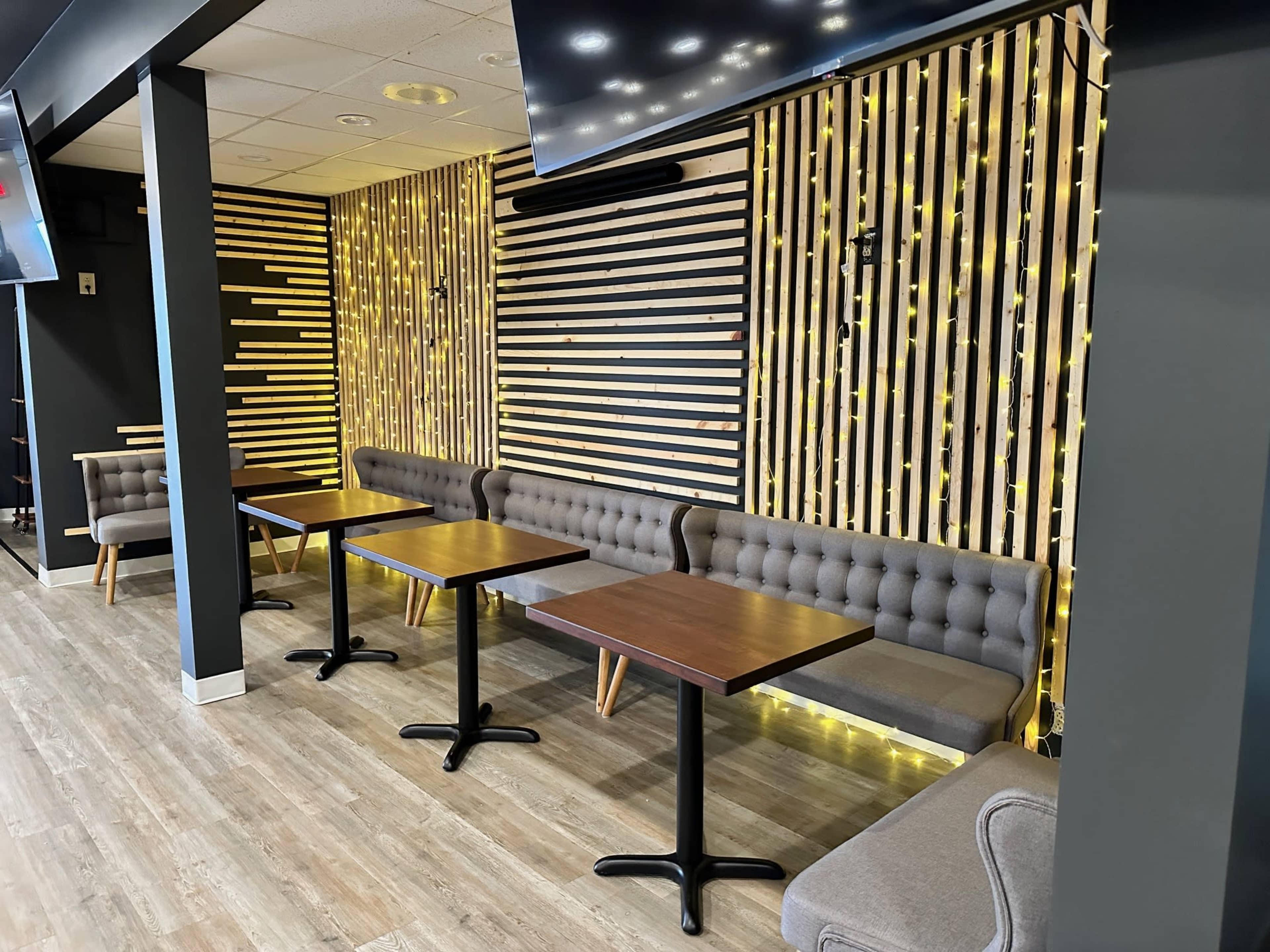 A modern café interior with tufted gray seating, wooden tables, and a decorative illuminated wall made of alternating wooden slats.