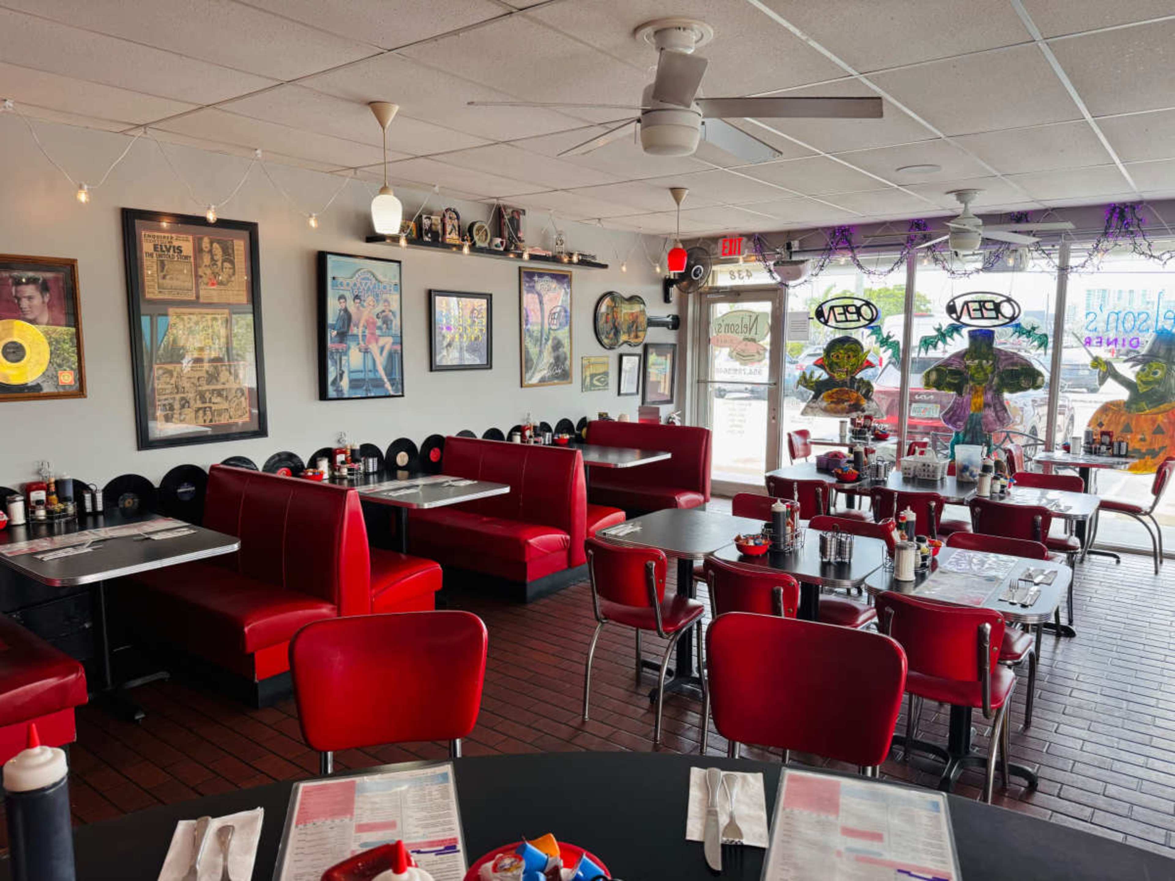 The image displays a diner interior featuring red vinyl booths and tables, decorated with framed artwork and vintage records on the walls.