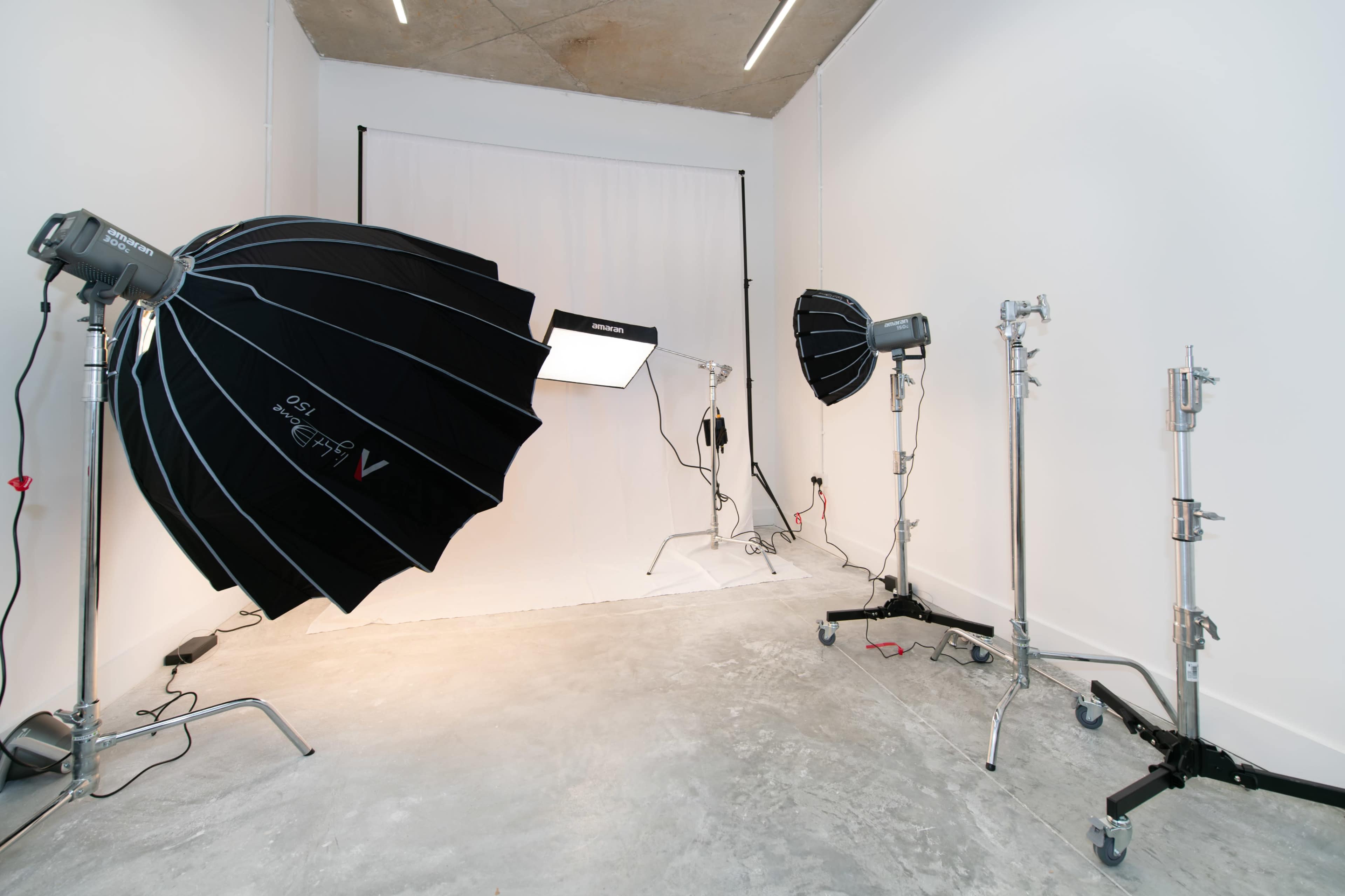A photography studio with several lighting setups, including softboxes and stands on a concrete floor.