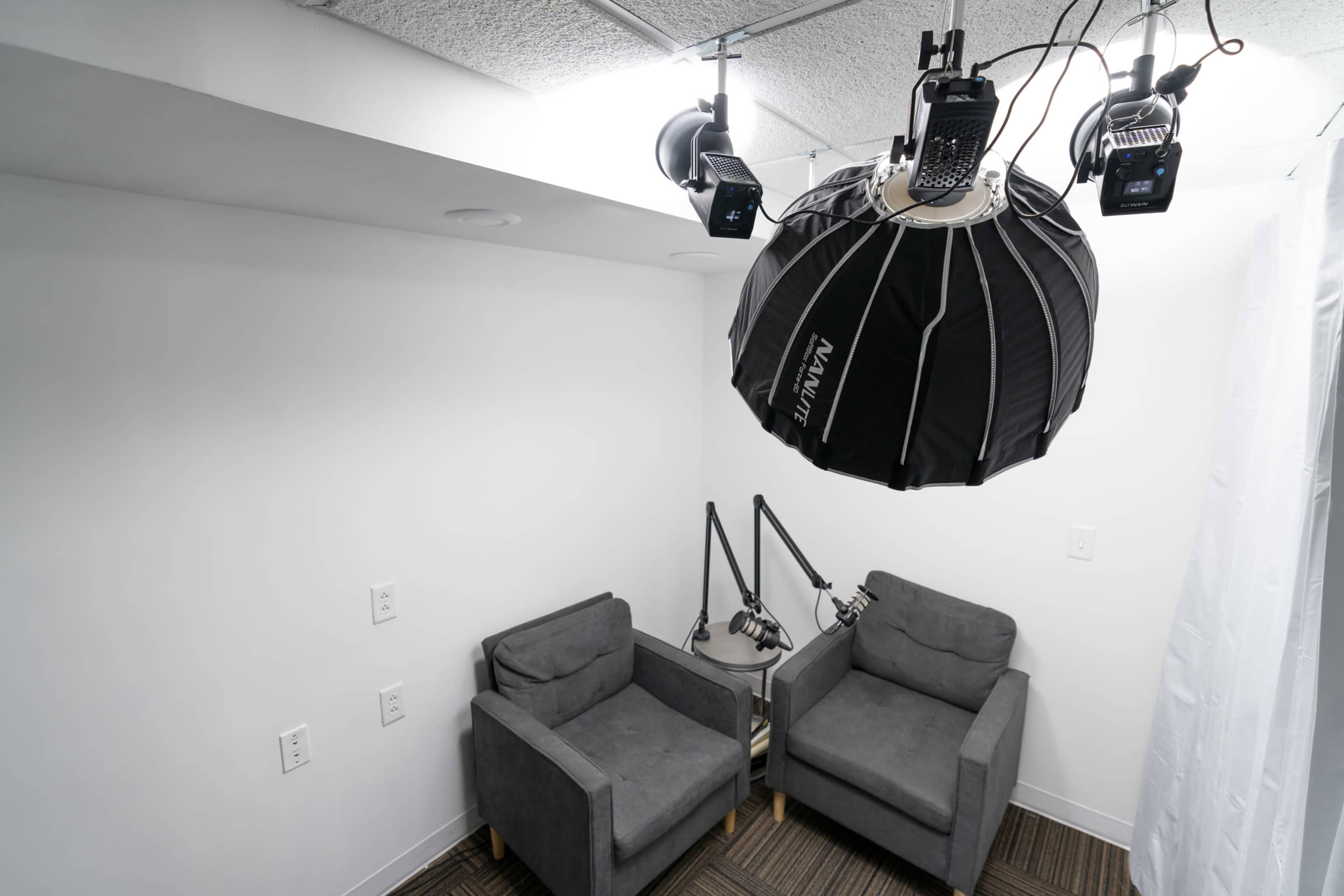 A small, well-lit studio space with two gray armchairs and a large softbox light hanging from the ceiling.