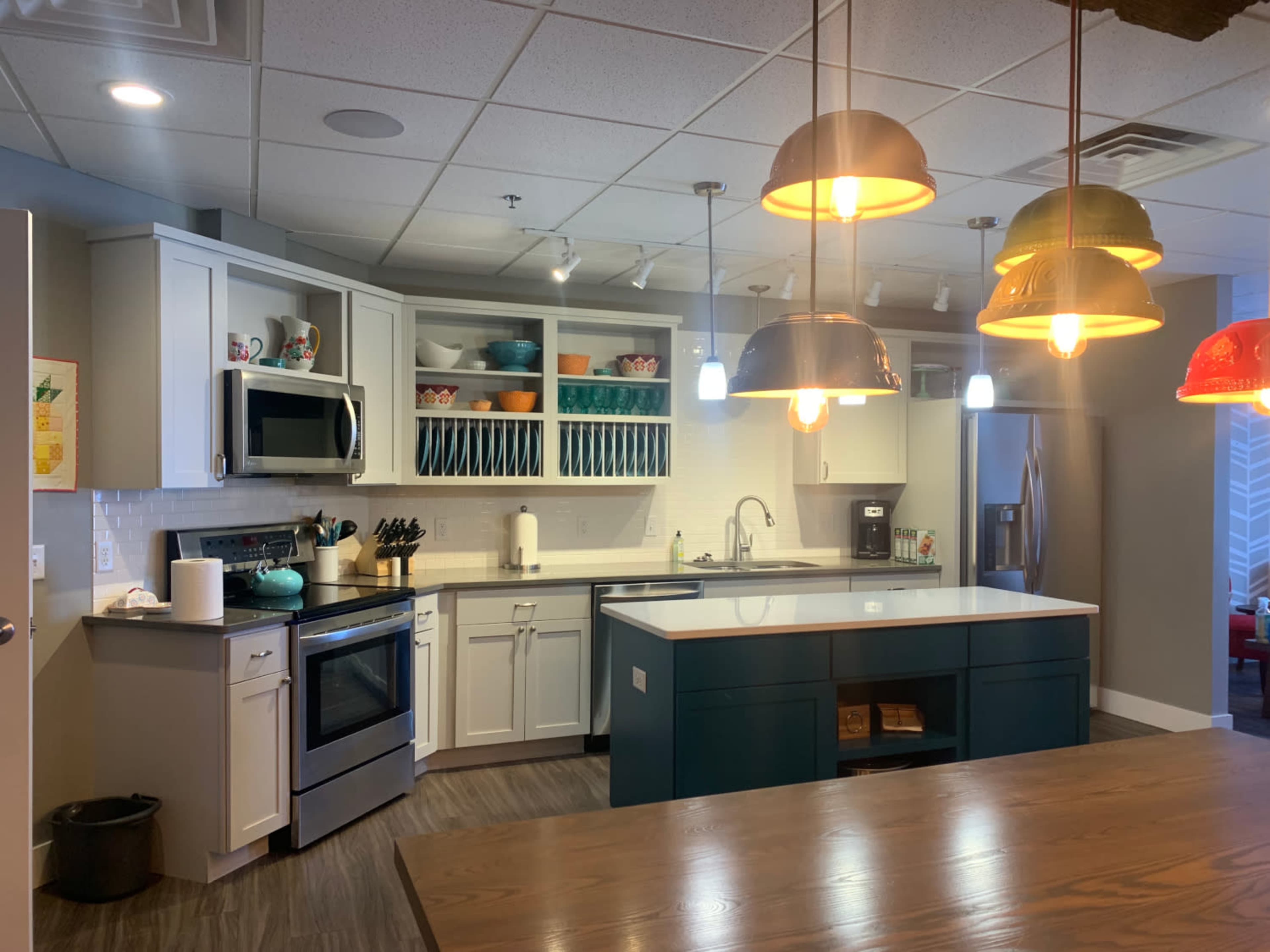 The image shows a modern kitchen with gray cabinets, a large island with a blue base, and pendant lights hanging above.