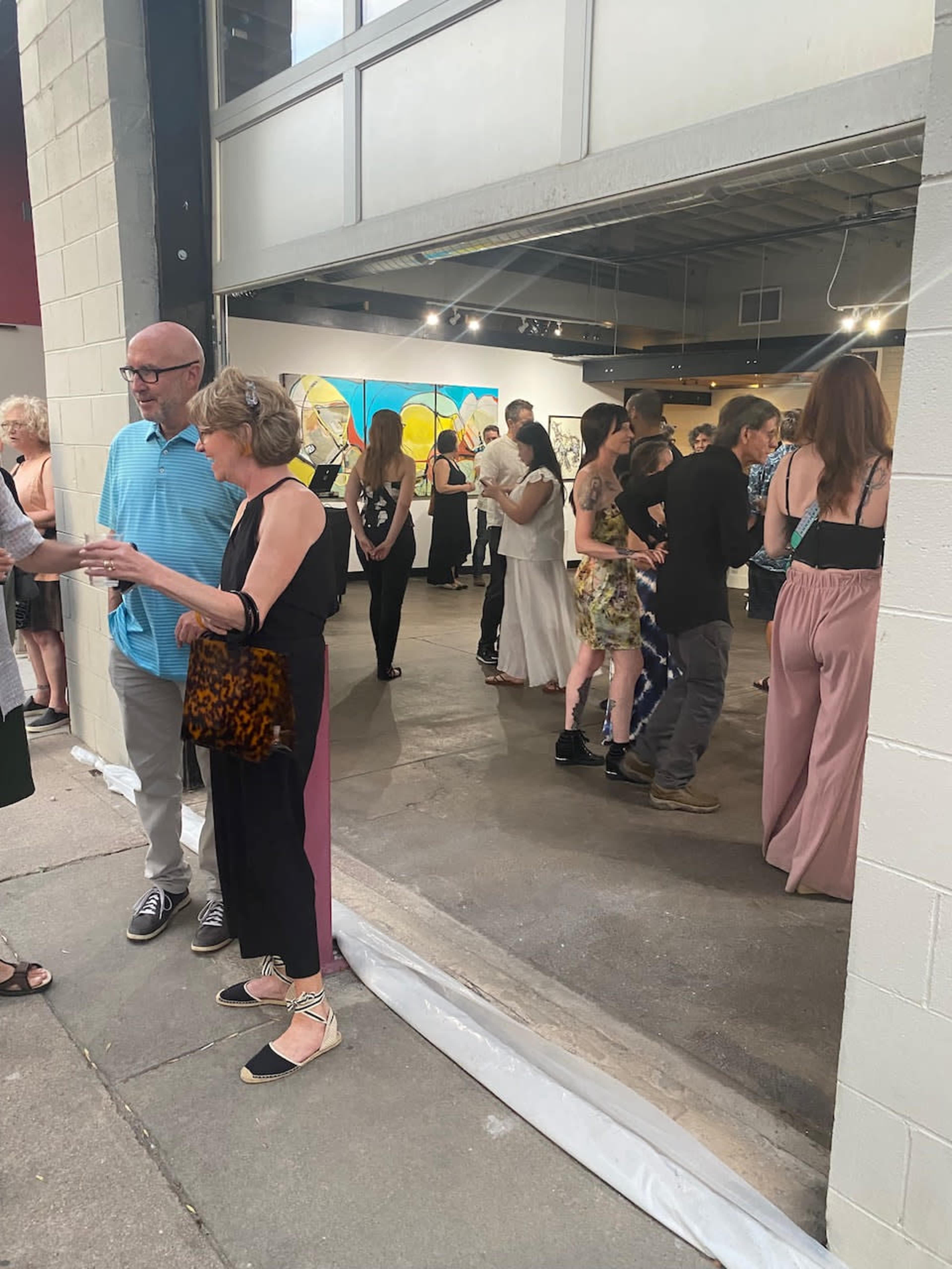 A group of people socialize inside an art gallery with colorful abstract paintings on the wall.