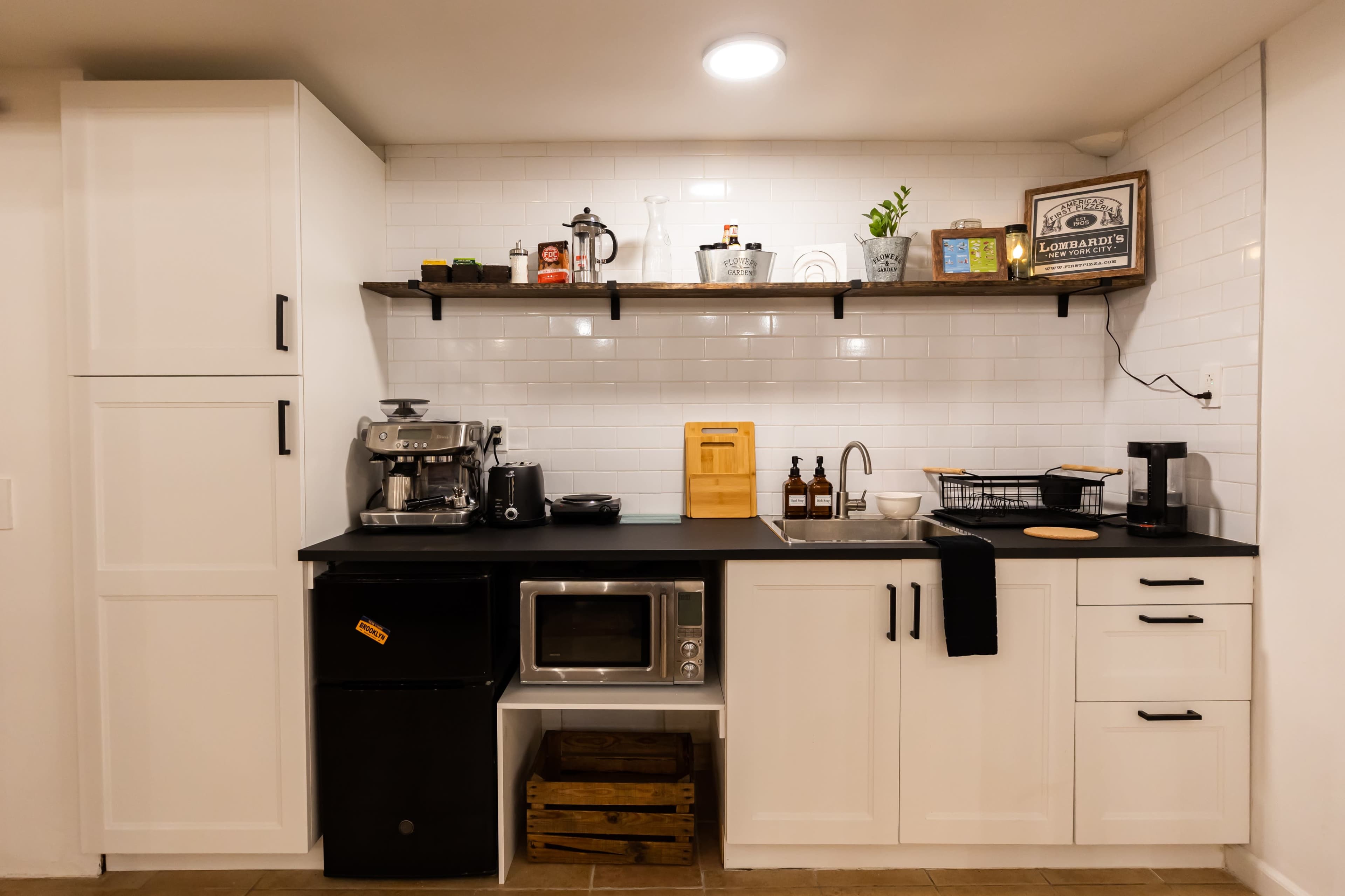 A modern kitchen setup with a black countertop, white cabinets, a microwave, a coffee machine, and open shelving displaying various items.