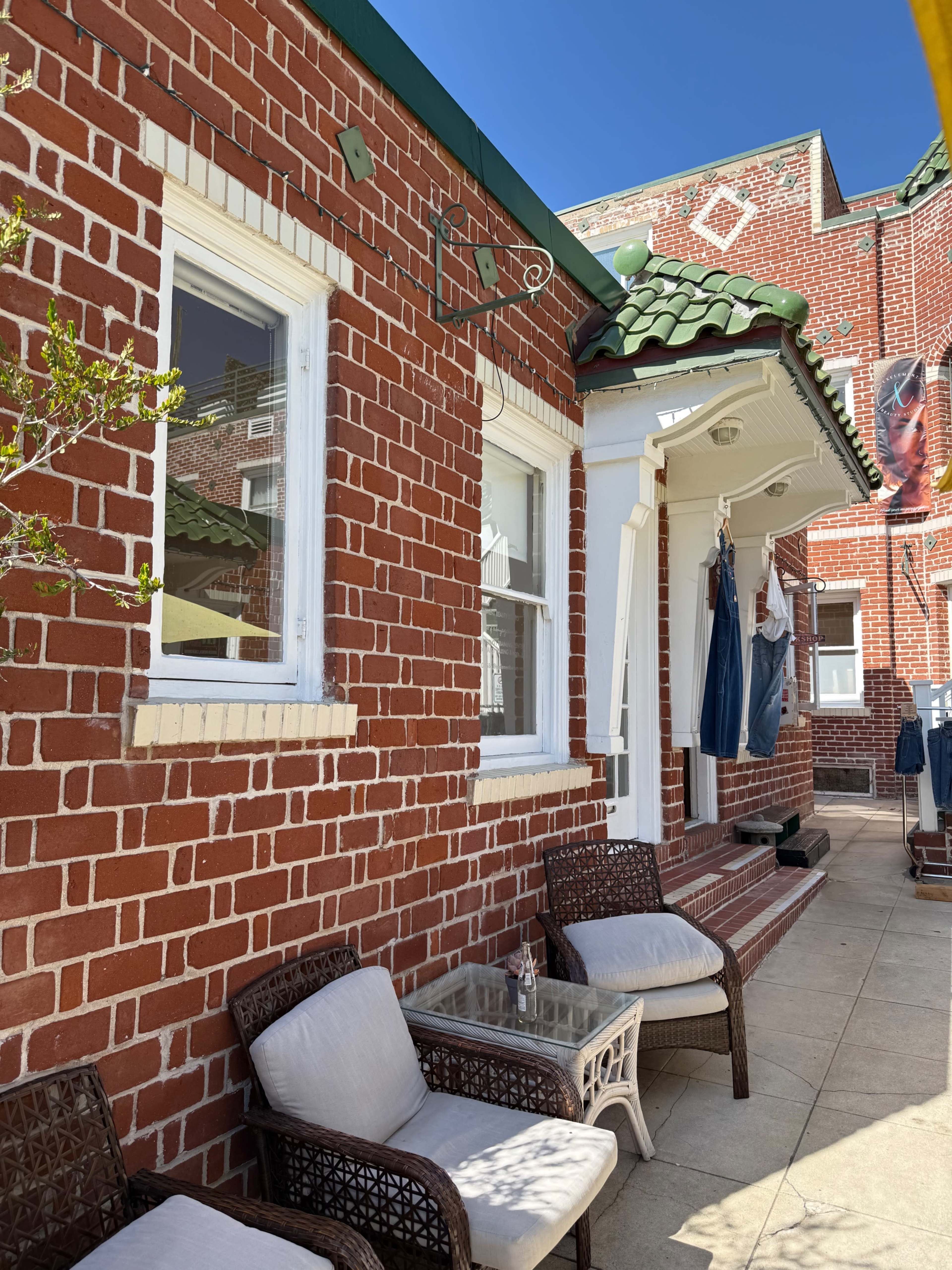 The image shows a brick patio area with two chairs and a small table near a building featuring a tiled roof and laundry hanging on a line.