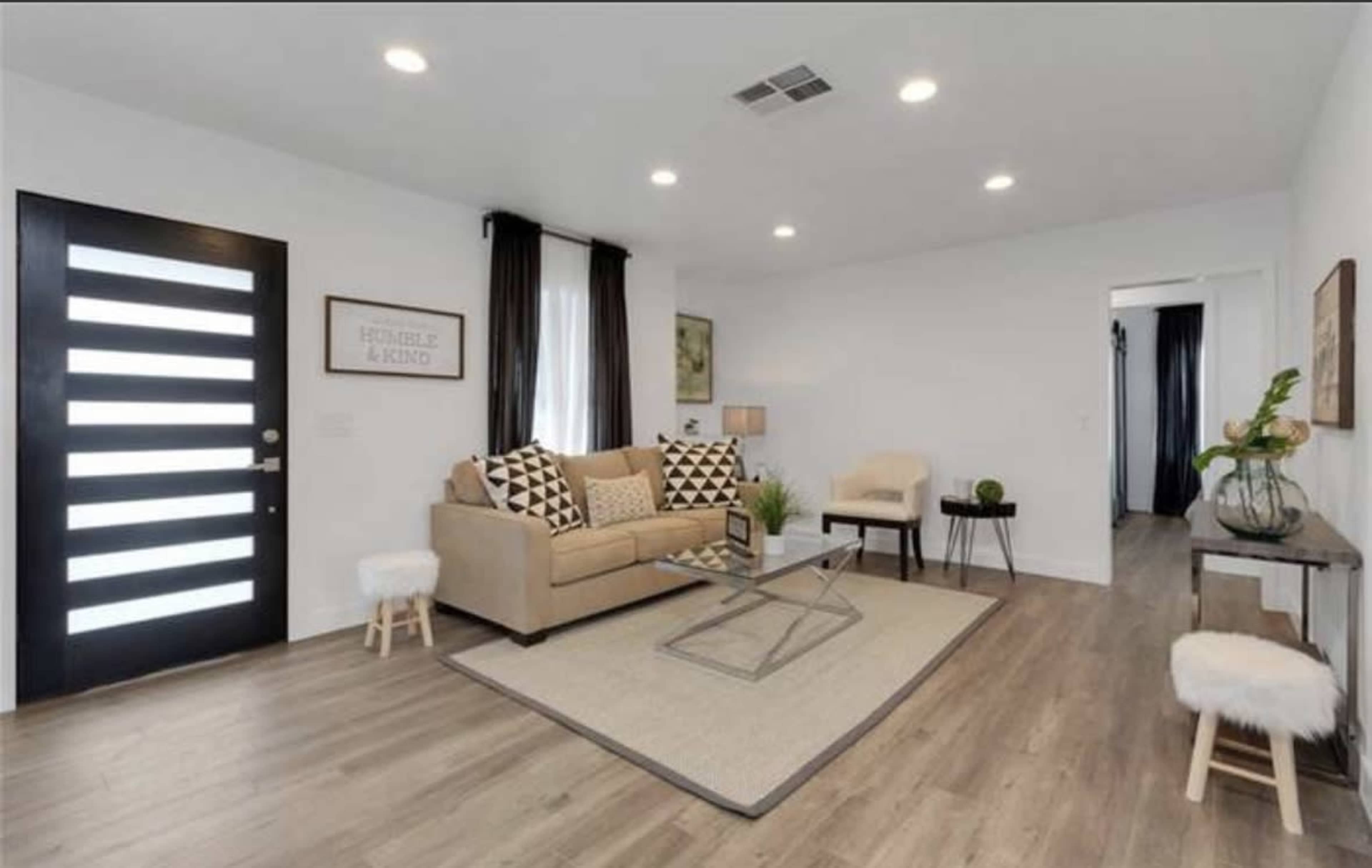 The living room features a neutral-colored sofa with patterned cushions, a coffee table on a large area rug, and a set of minimalist decor elements.