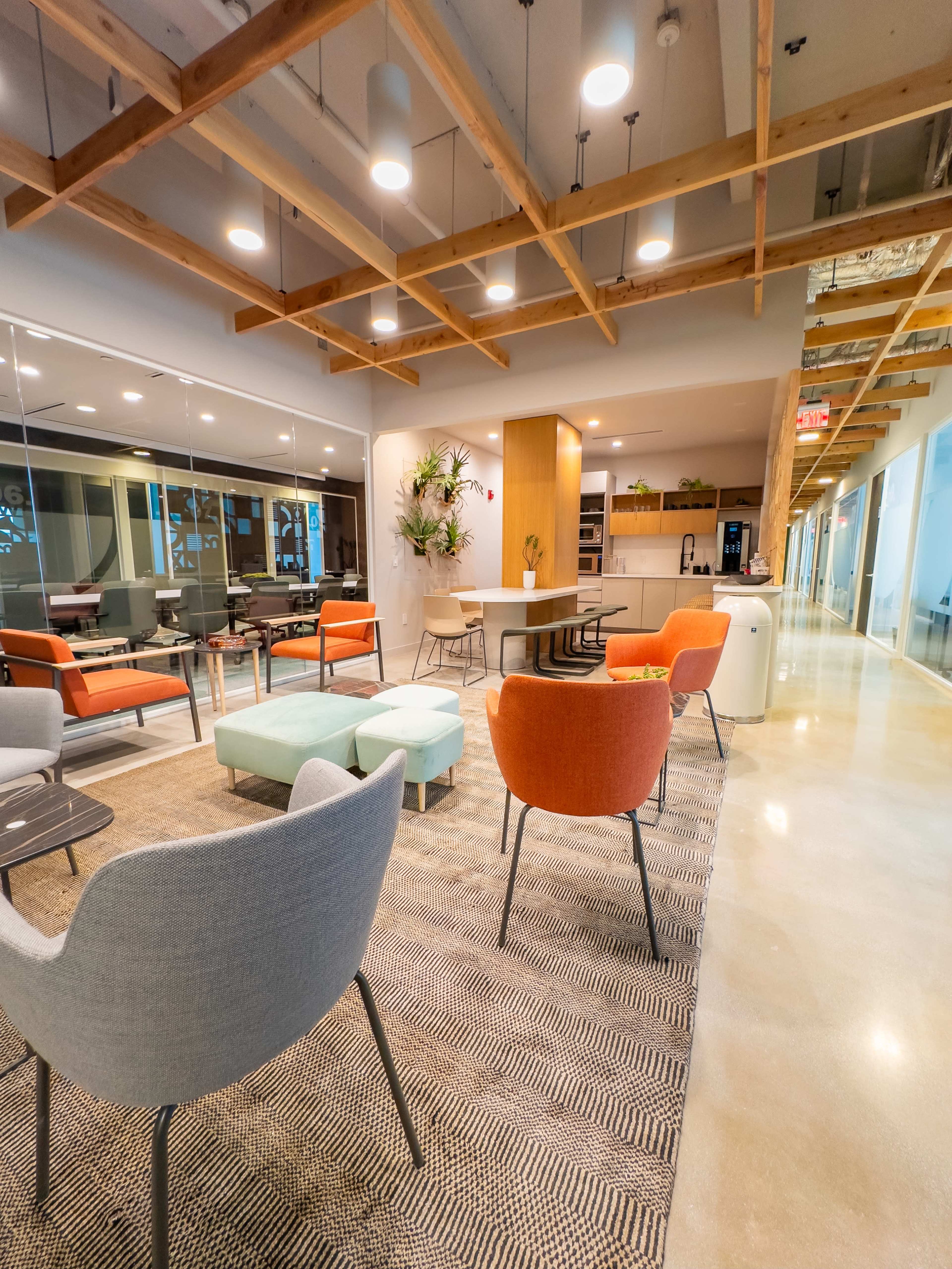 A modern office lounge area with colorful seating, a large communal table, and glass partitions.