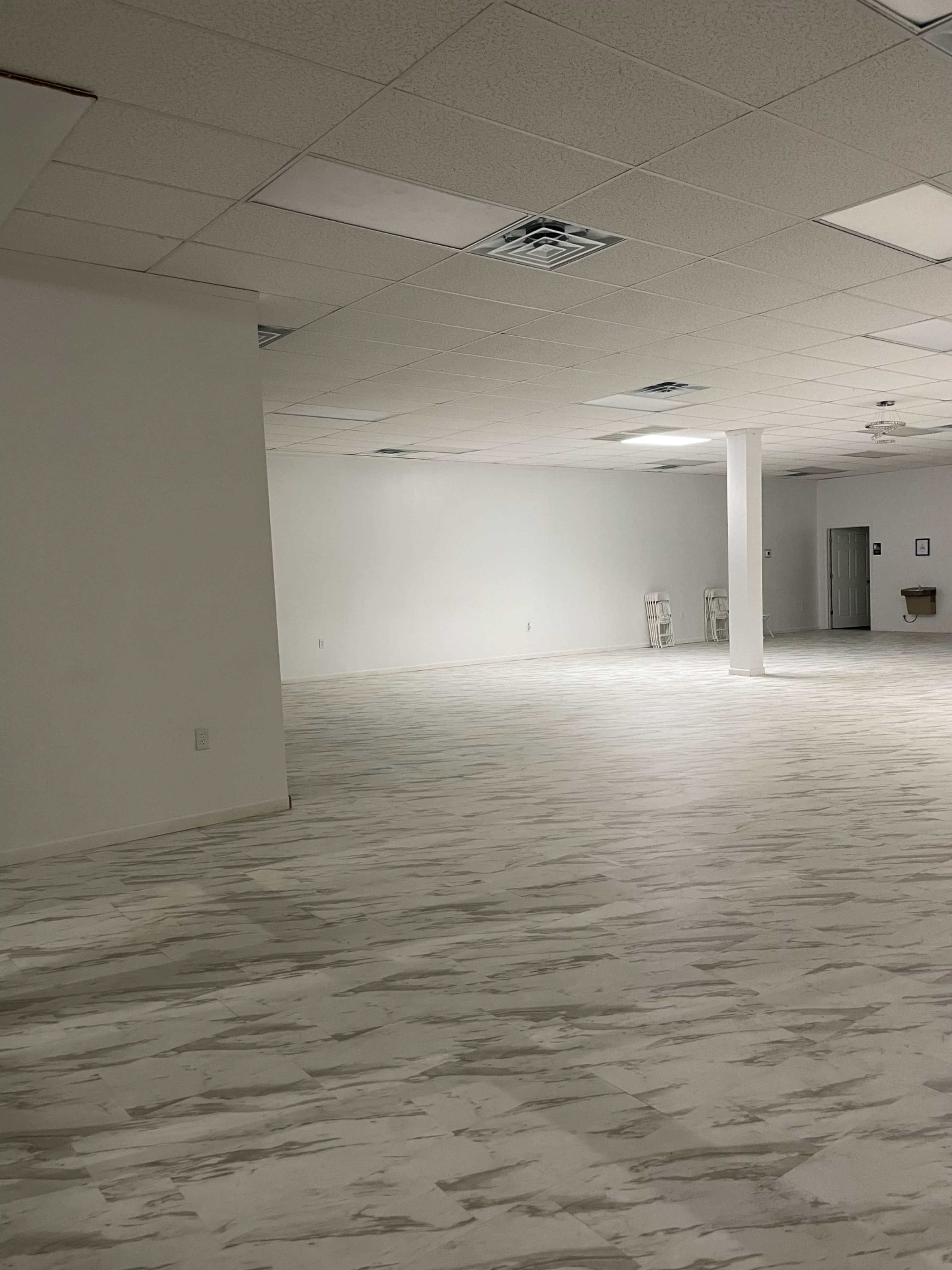 A spacious, empty room with white tile flooring and minimal furniture against plain walls.