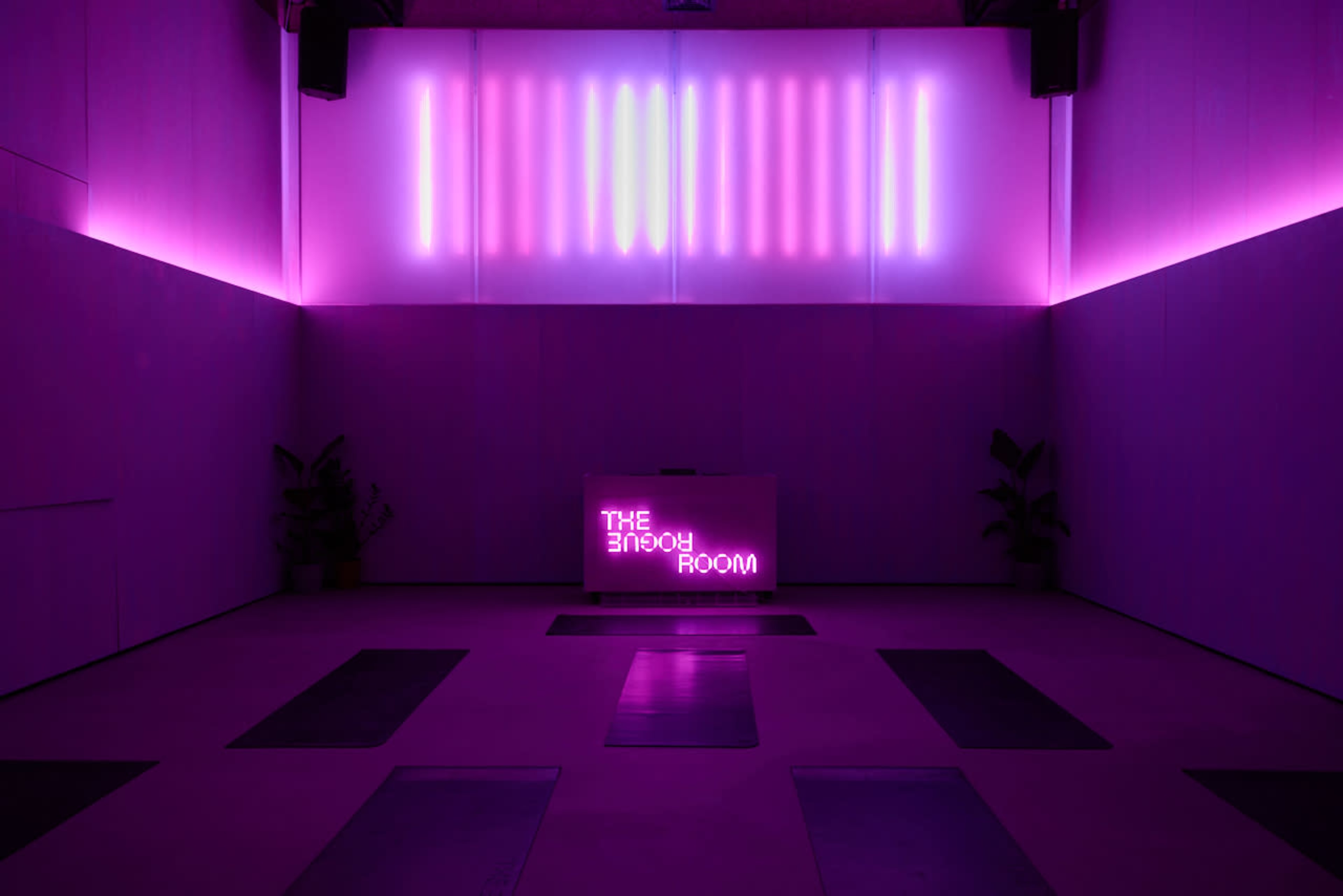 The image shows a dimly lit room with purple lighting, featuring a sign that reads "THE EMO ROOM" and several exercise mats arranged on the floor.
