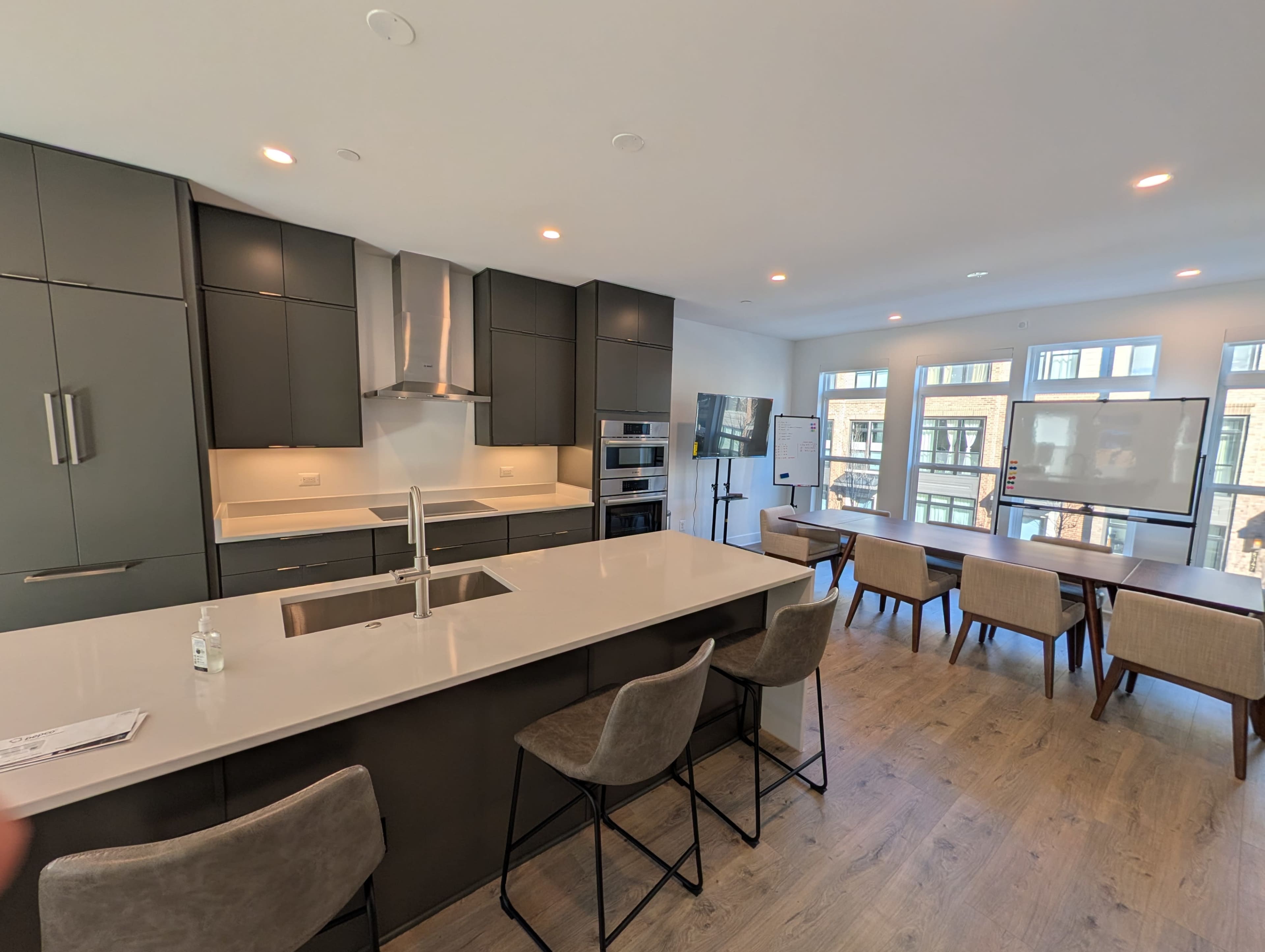 The image shows a modern kitchen and dining area with dark cabinetry, stainless steel appliances, and a large island with seating.