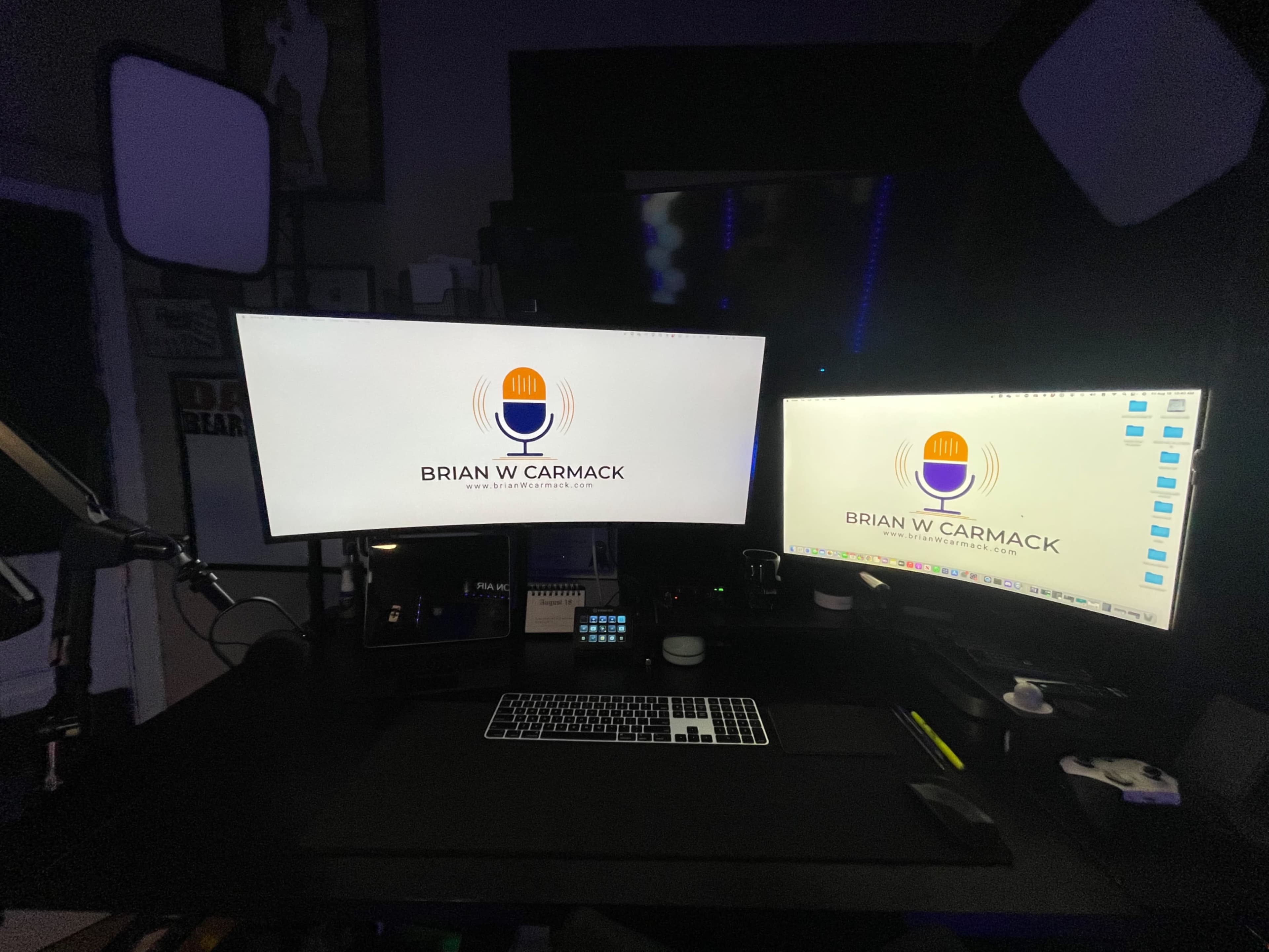 A dual monitor setup on a desk with the name "BRIAN W CARMACK" and a microphone logo displayed on both screens.