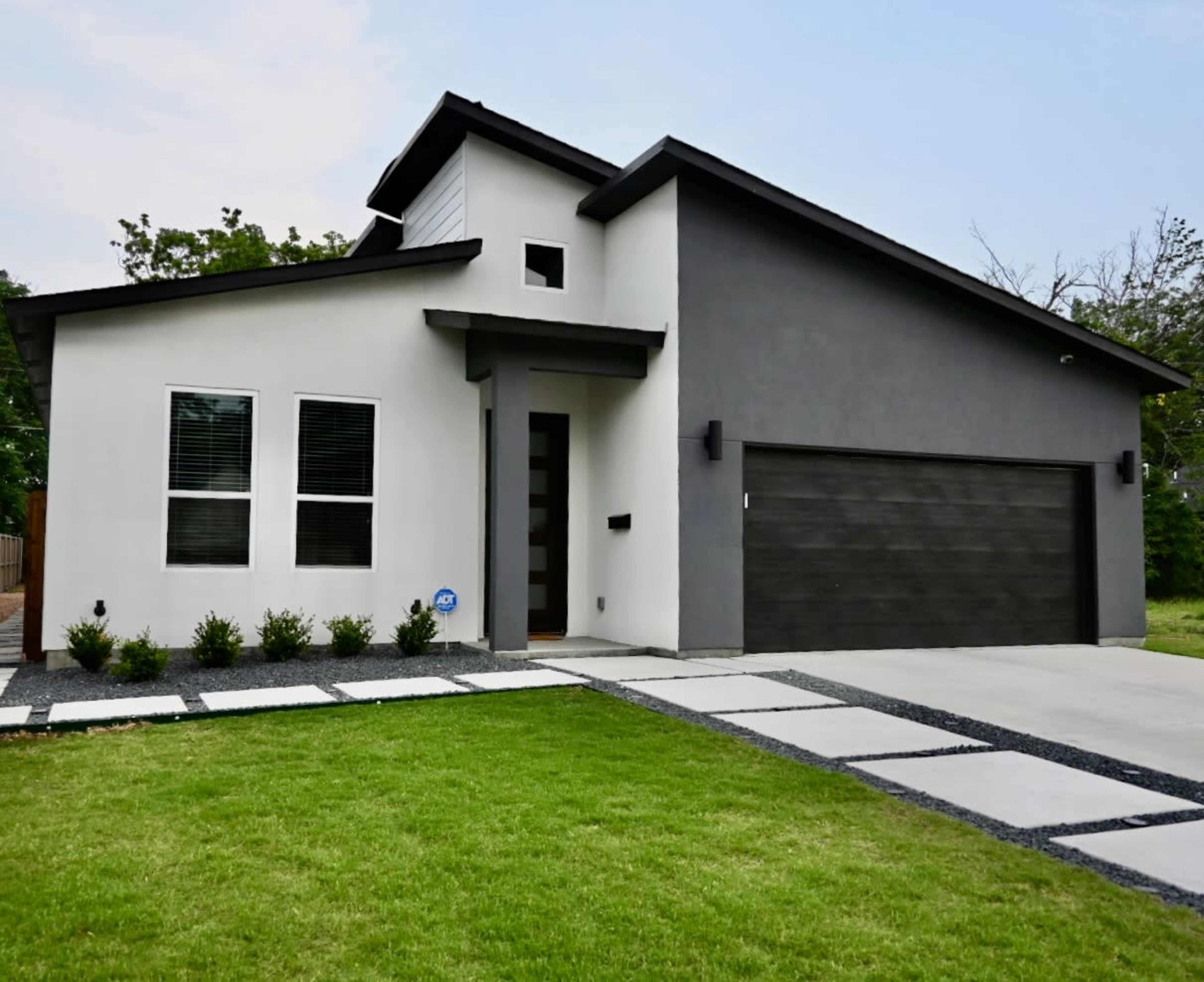 A modern house with a two-tone exterior, featuring large front windows, a single-car garage, and a landscaped yard with a stone pathway.