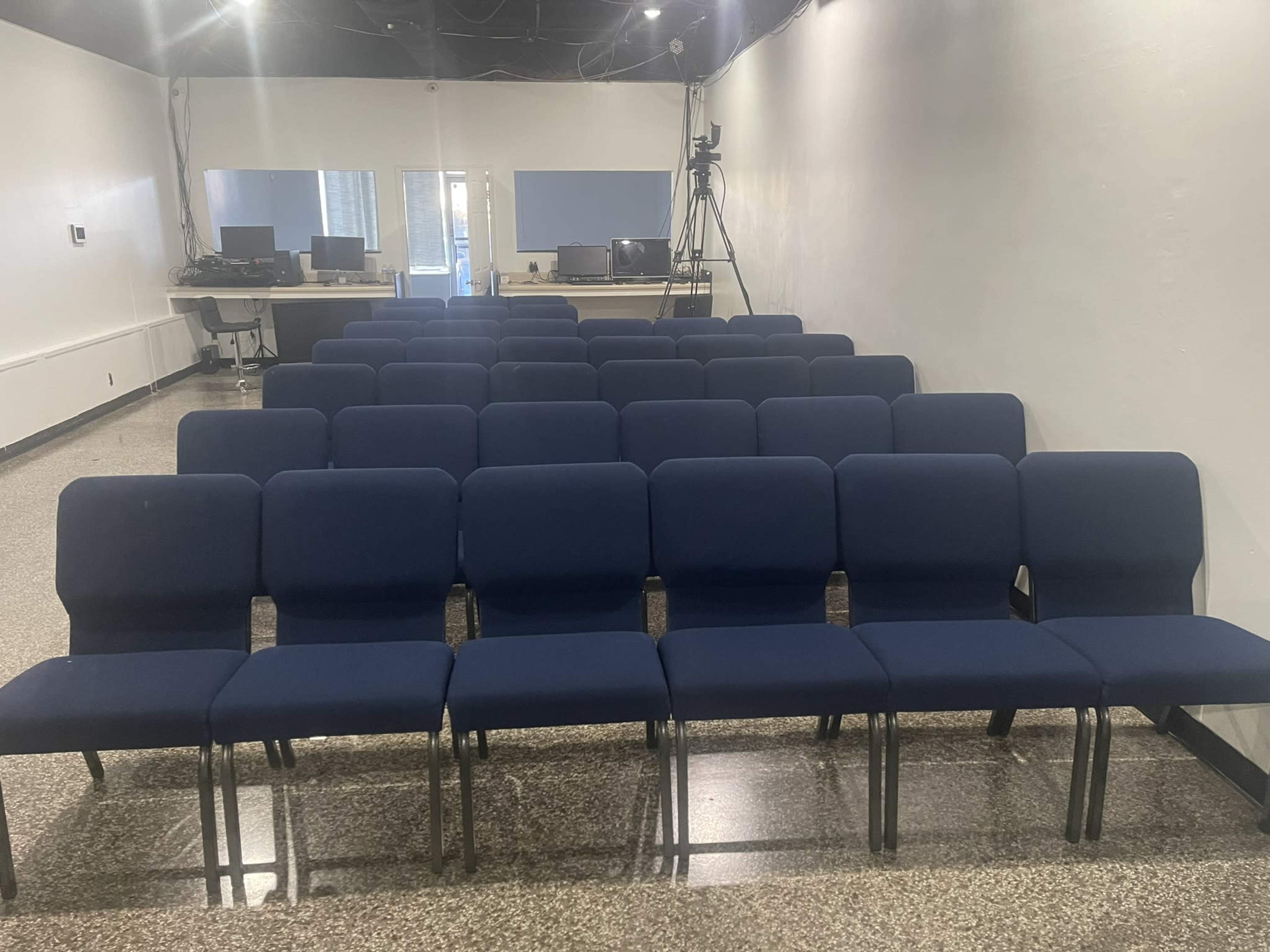 A row of blue chairs arranged in a semi-circle in a room with a polished floor and computer stations in the background.