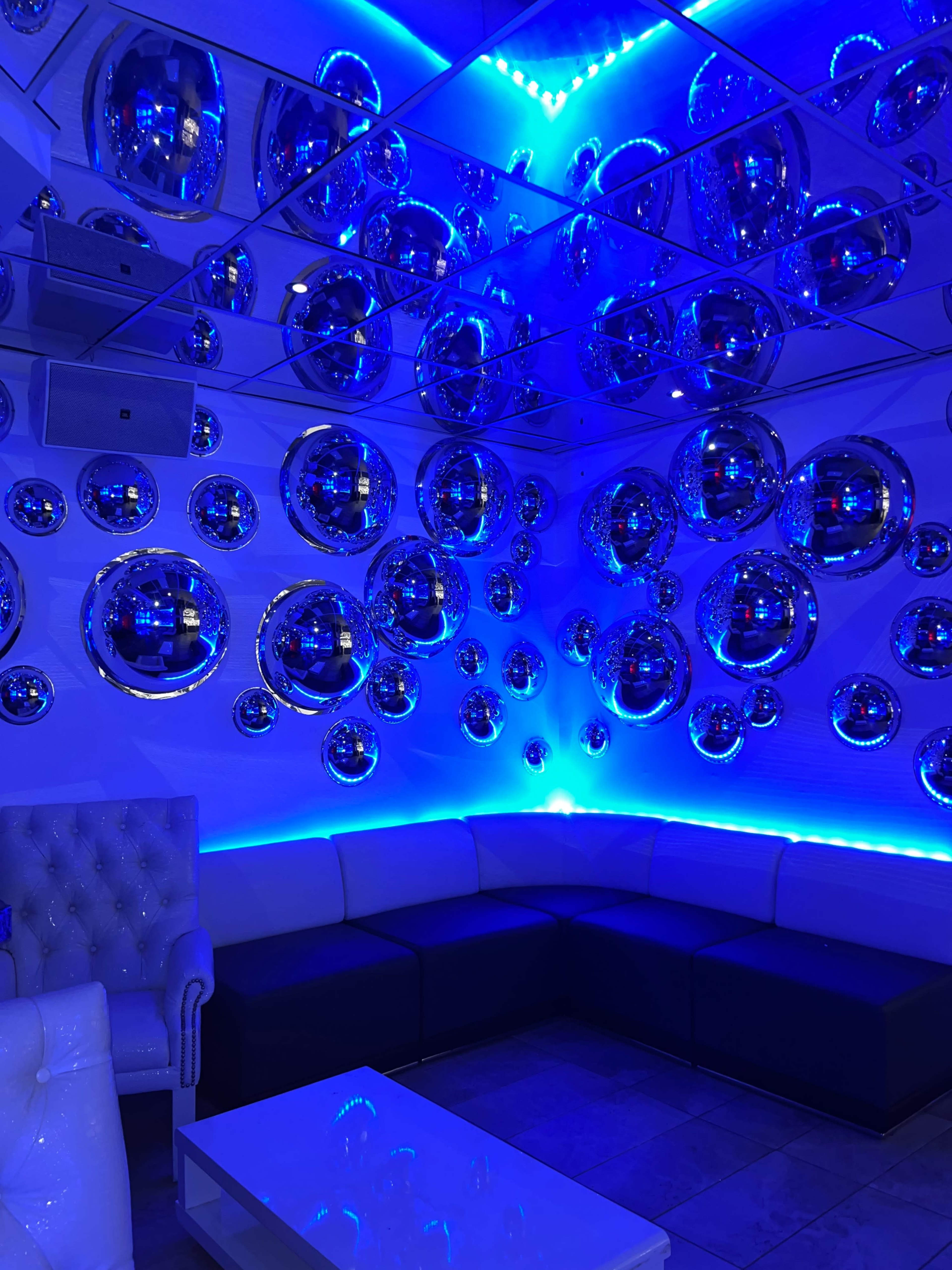 The room features a modern design with a white and dark couch, a white table, and circular mirrors framed in chrome, illuminated by blue LED lights.