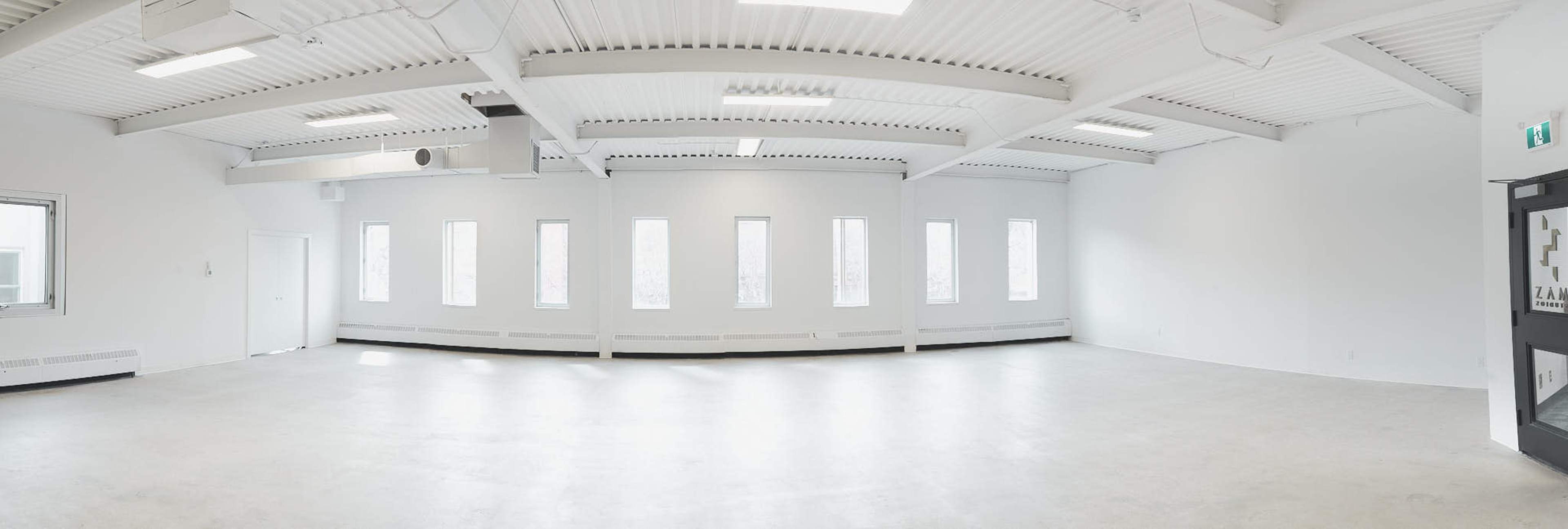 A large, empty room with white walls, a concrete floor, and several windows along one side.