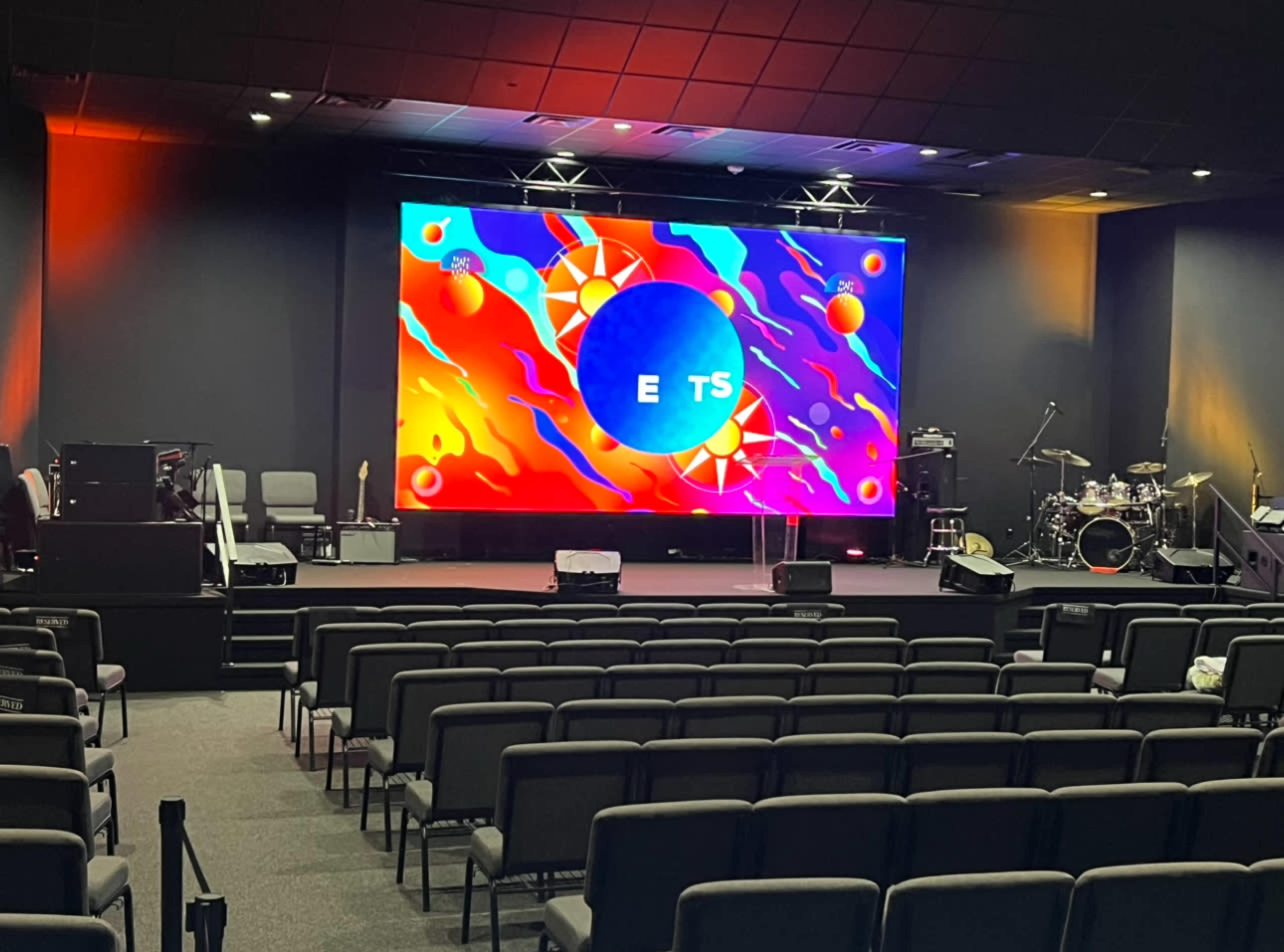 A stage setup in an auditorium with a large, colorful digital screen in the background and empty rows of seats facing the stage.