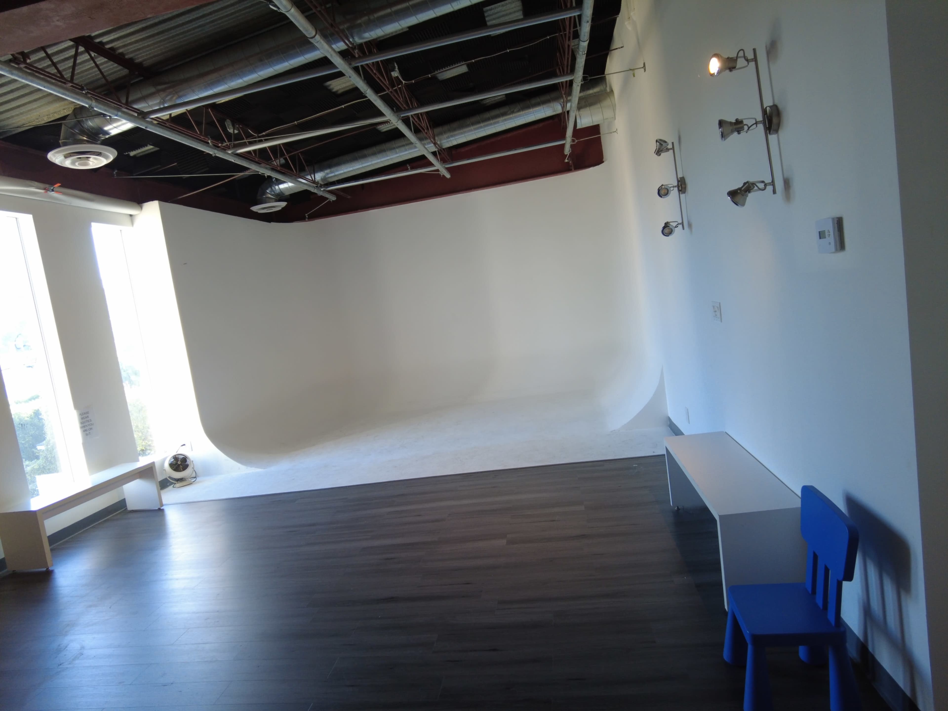 The image shows a spacious, well-lit studio with a white curved backdrop and a blue chair positioned beside a white bench.