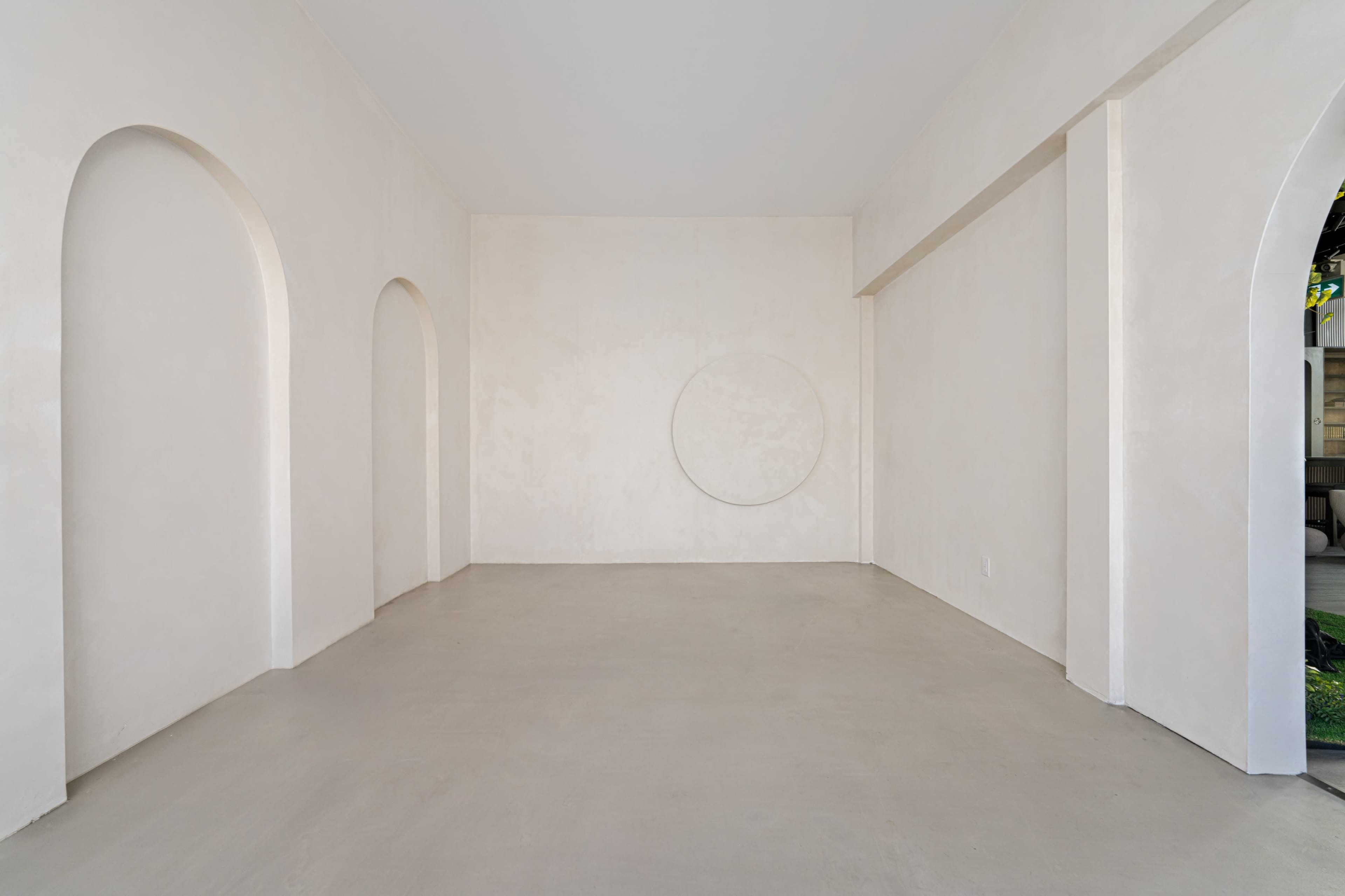 A minimalistic interior room with curved archways and a round wall feature on a plain, light-colored wall.