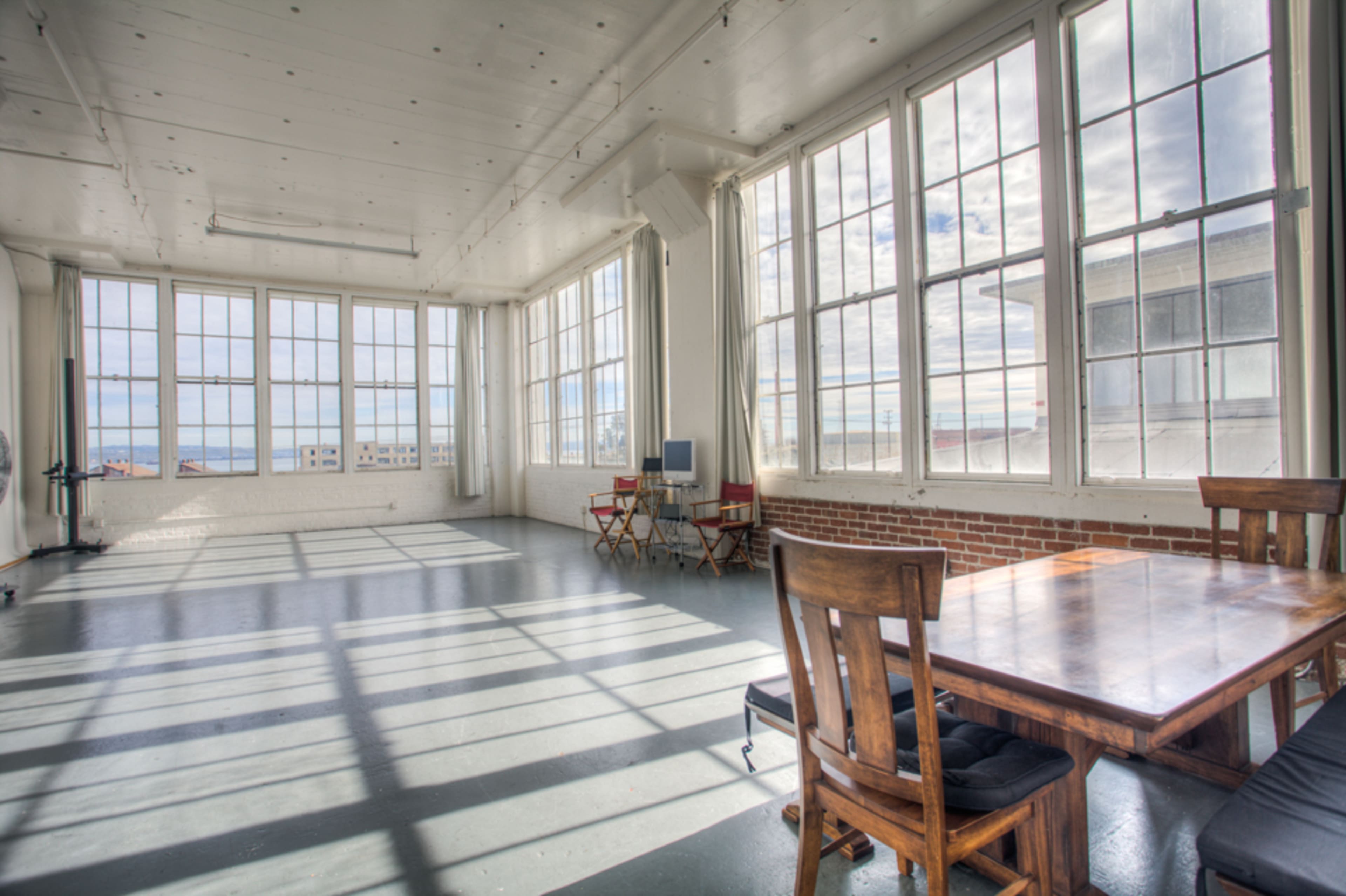 A spacious room with large windows, a wooden dining table, and two chairs, allowing natural light to illuminate the space.