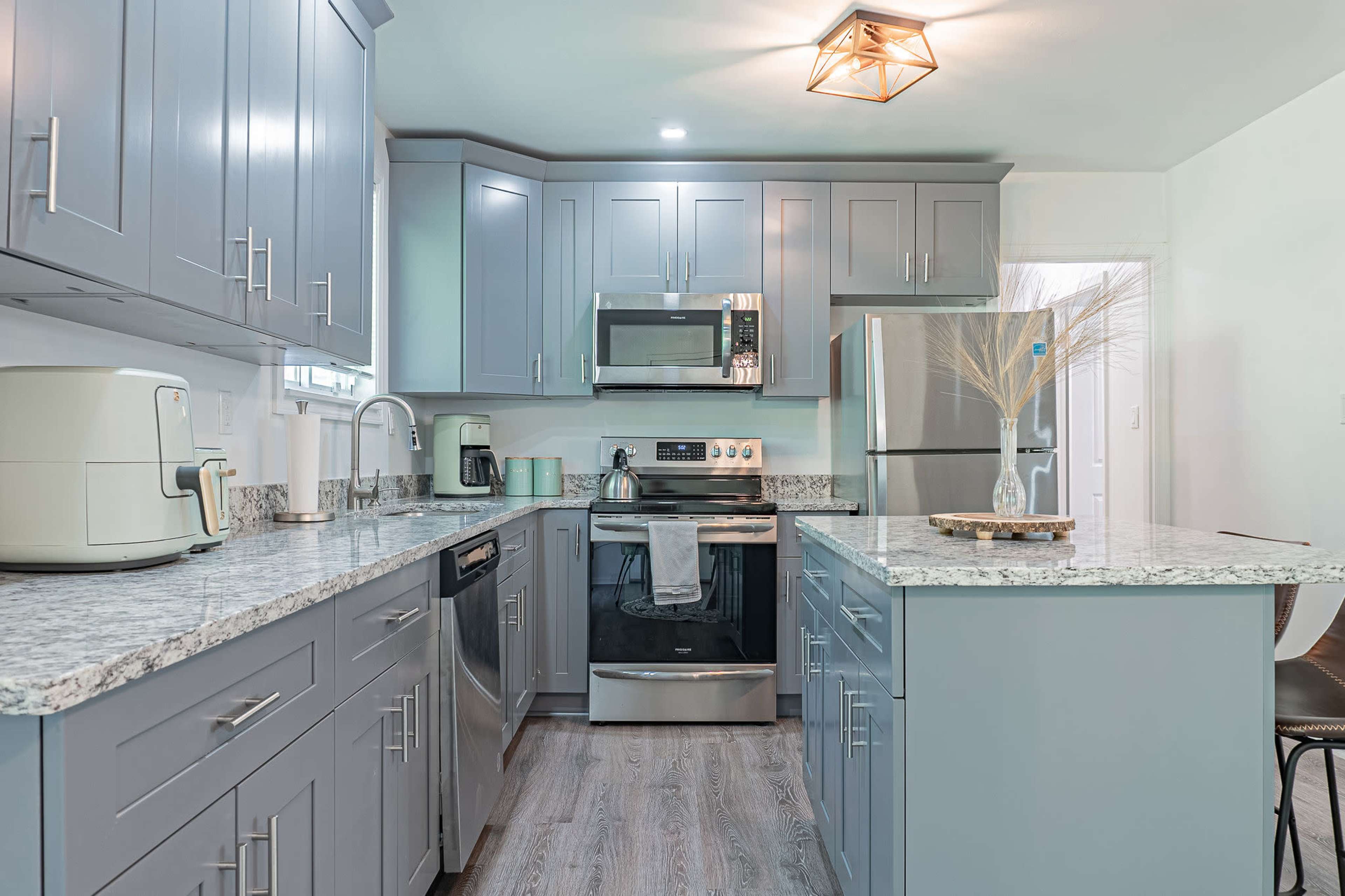 A modern kitchen with gray cabinets, a stainless steel refrigerator, and granite countertops.