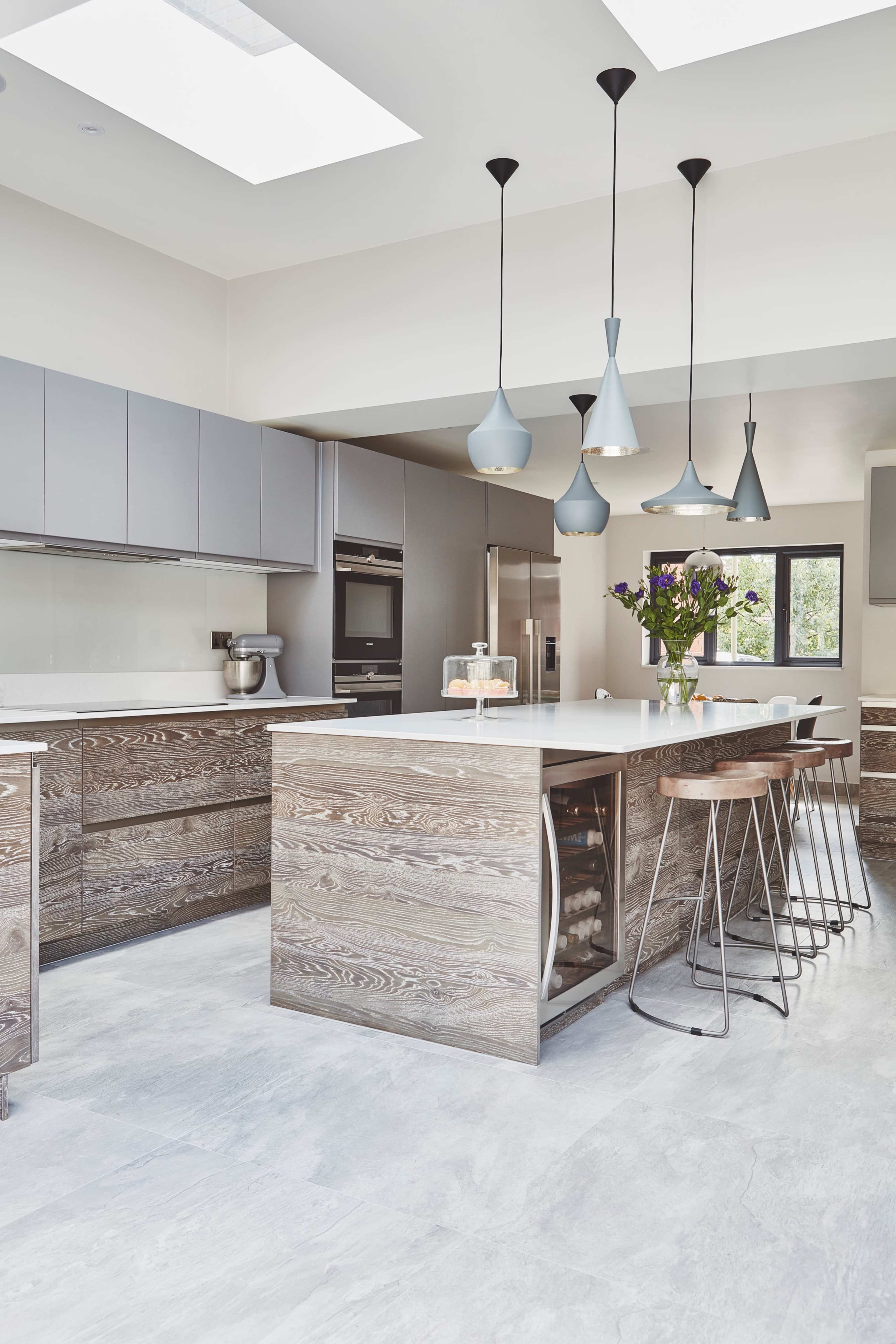 A modern kitchen features sleek cabinetry, a central island with seating, and pendant lighting above.
