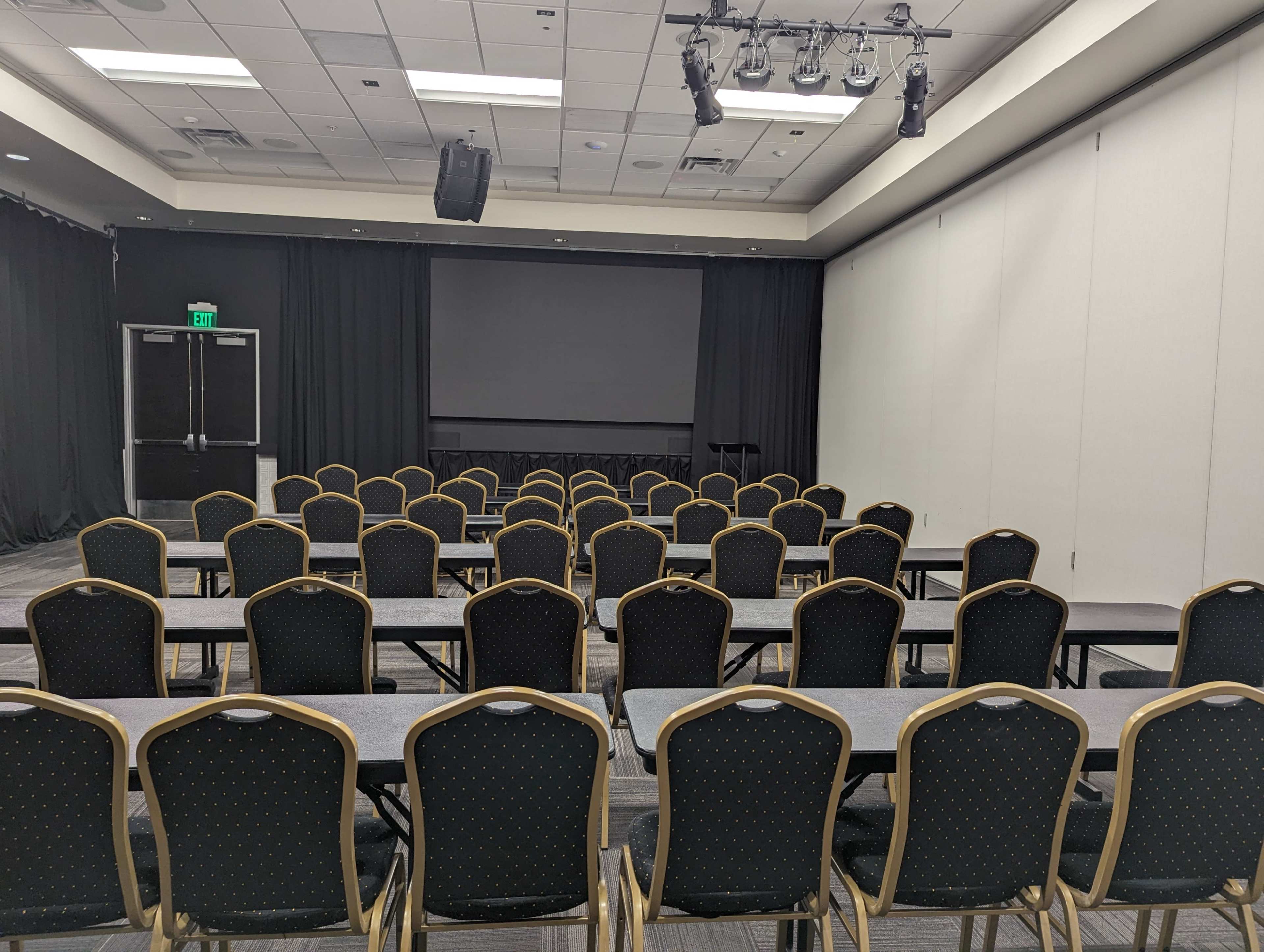 A conference room set up with rows of chairs and tables facing a large screen.