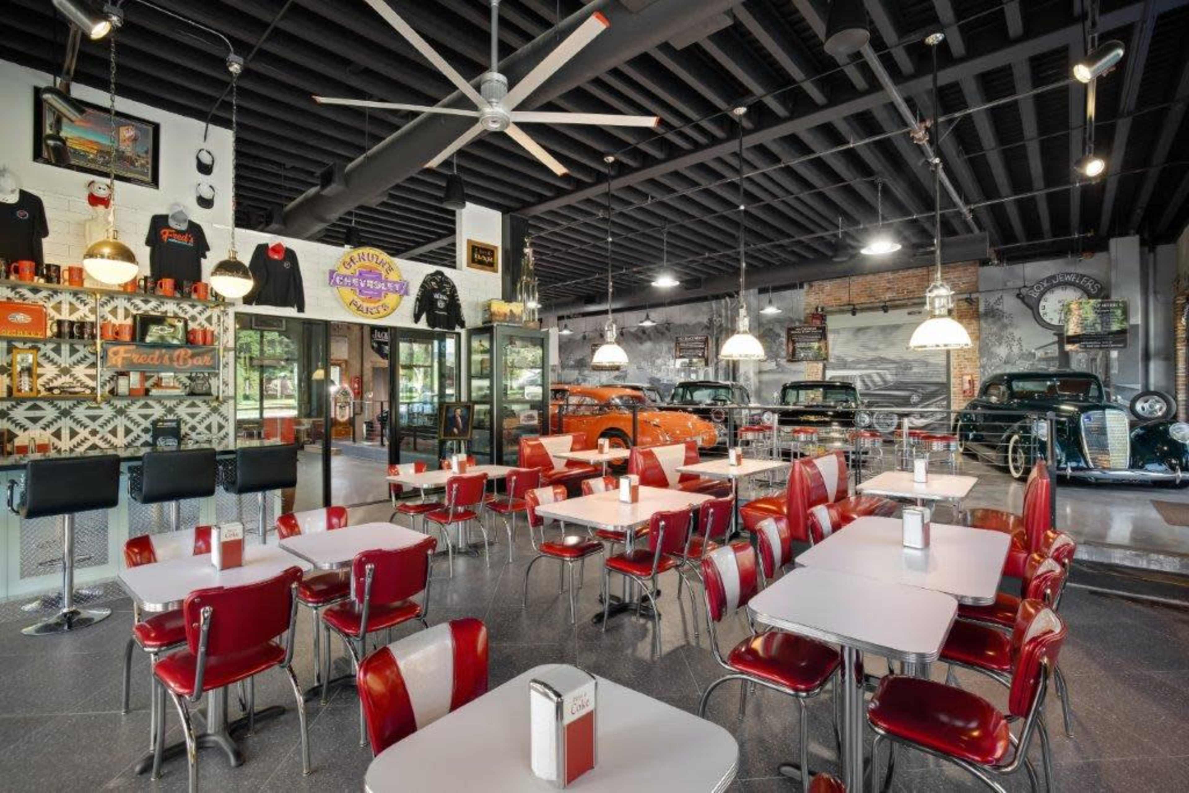 The scene shows a retro diner with red and white seating, a counter area, and vintage cars displayed in the background.