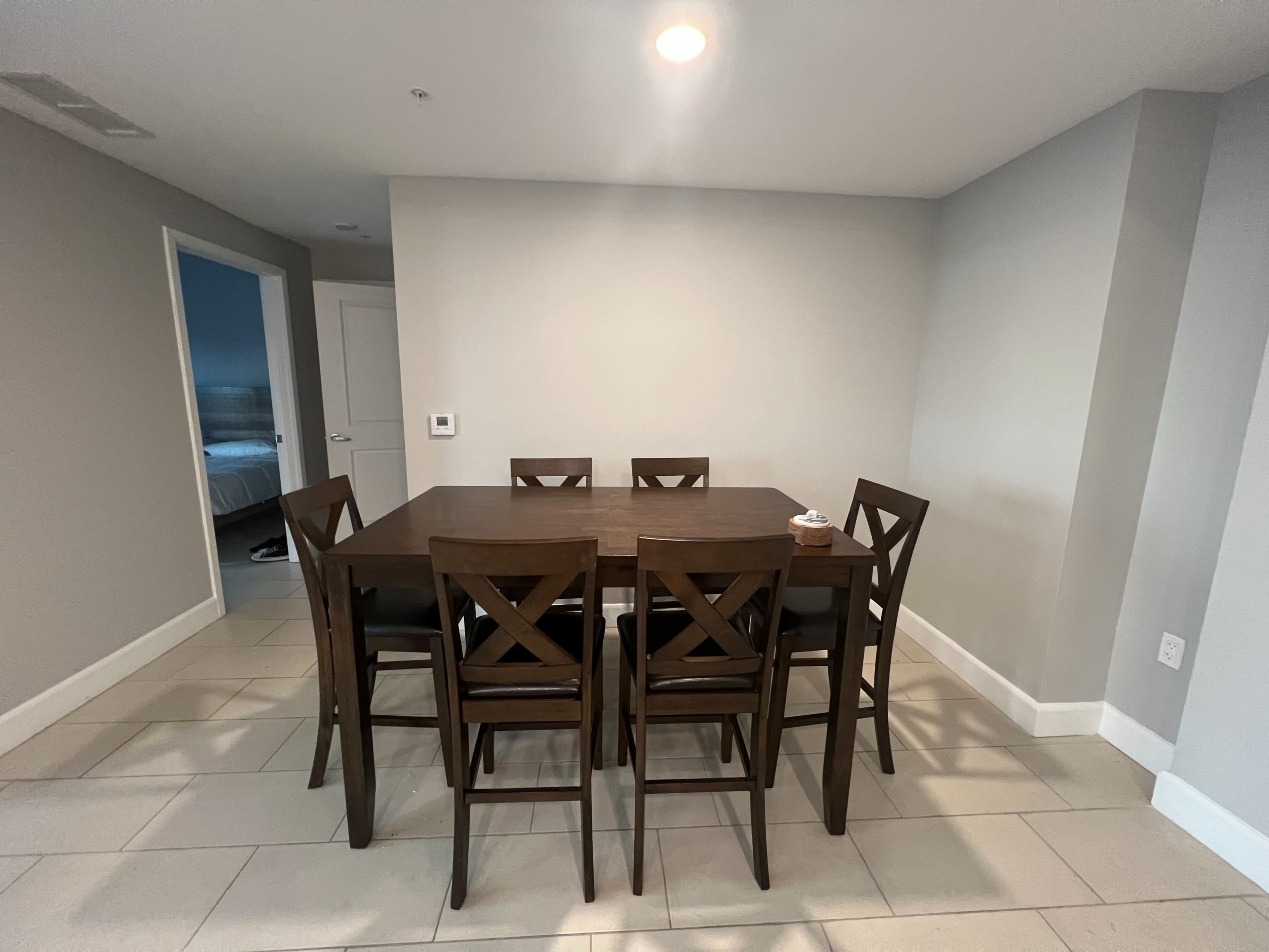 A rectangular wooden dining table surrounded by six high-backed chairs is positioned in a well-lit, minimalist room.