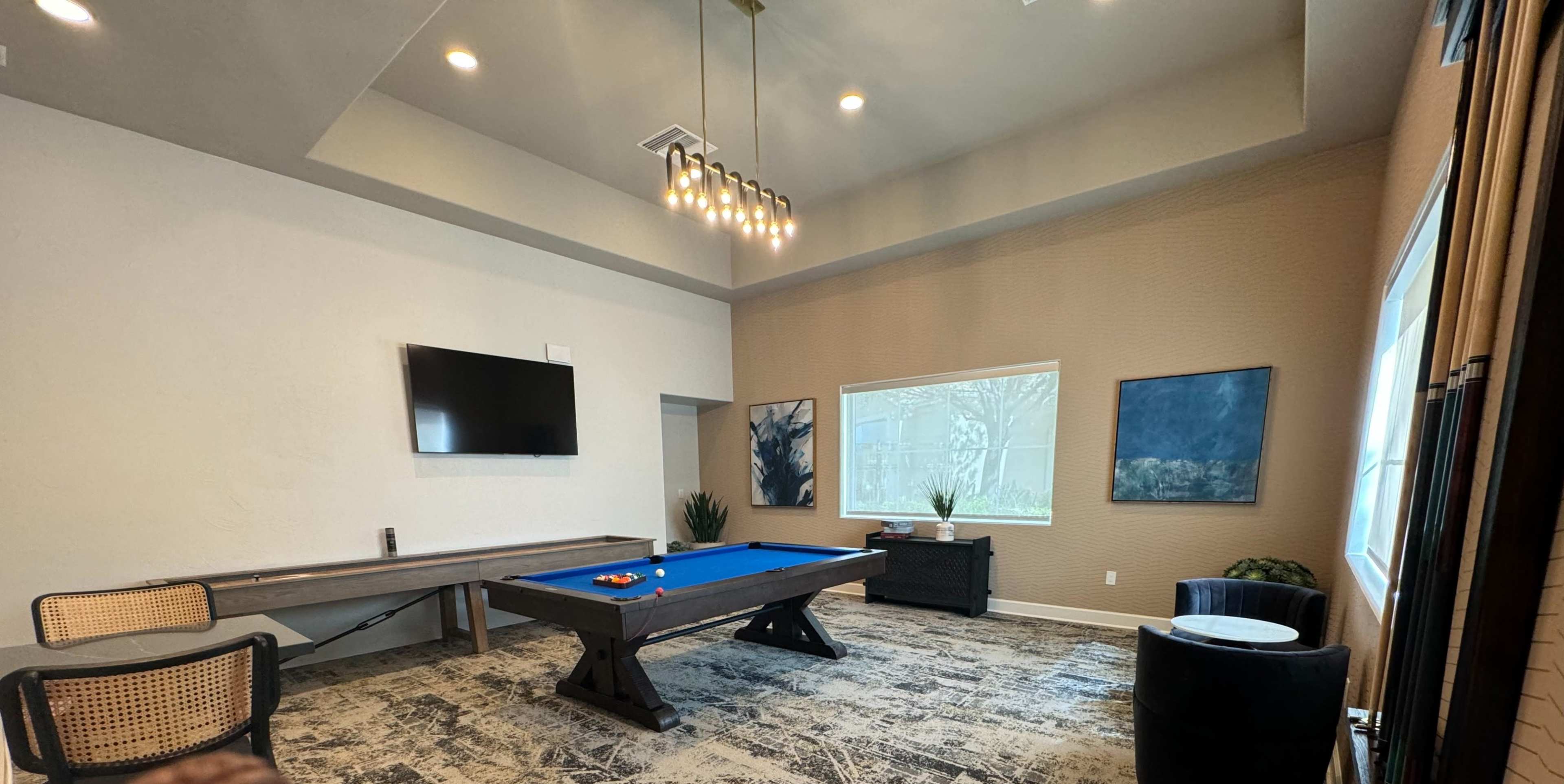 The room features a pool table, a television mounted on the wall, and two artworks displayed near a large window.