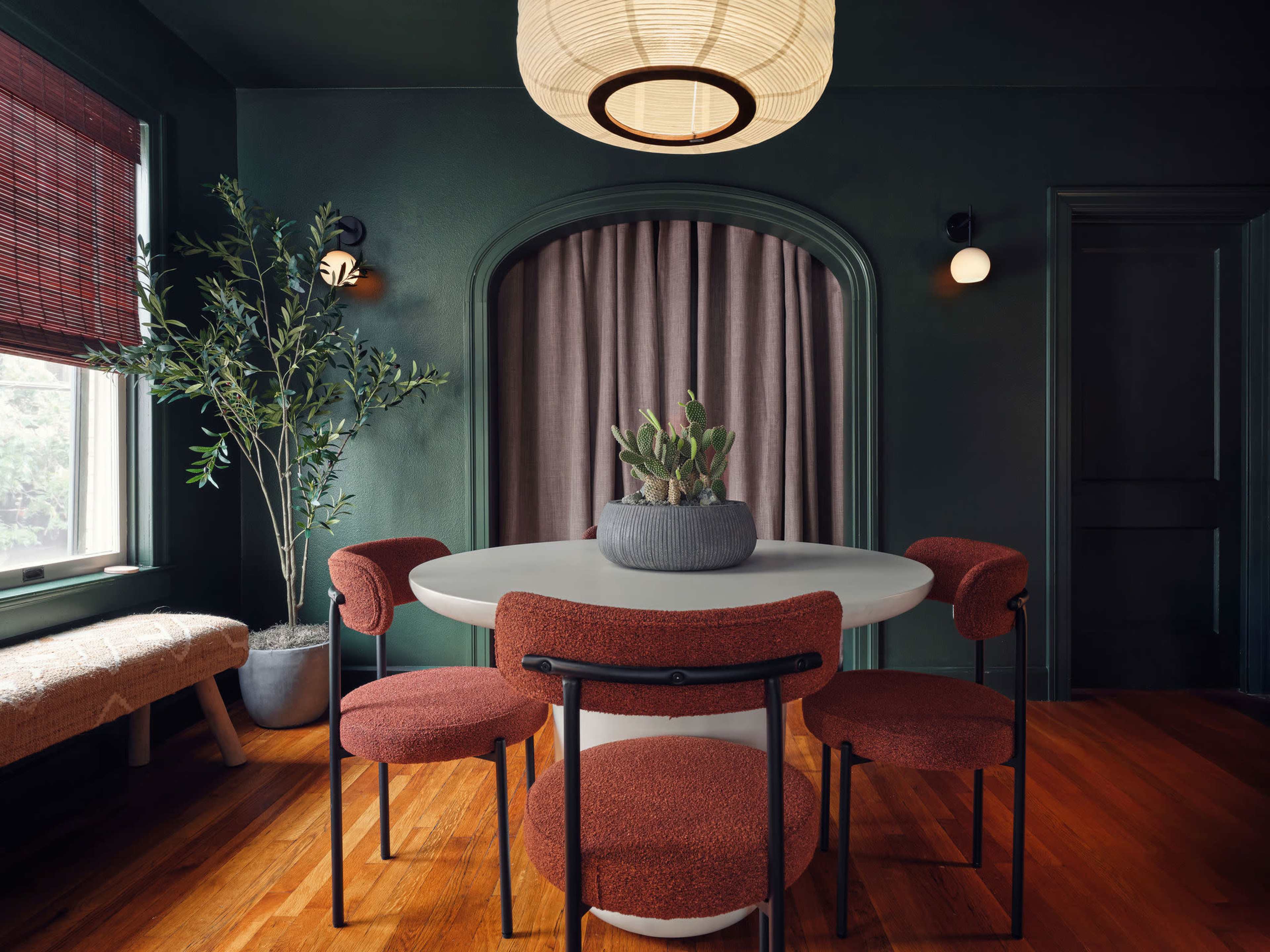 A modern dining area features a round table surrounded by four curved chairs, a potted plant in the center, and warm wooden flooring.