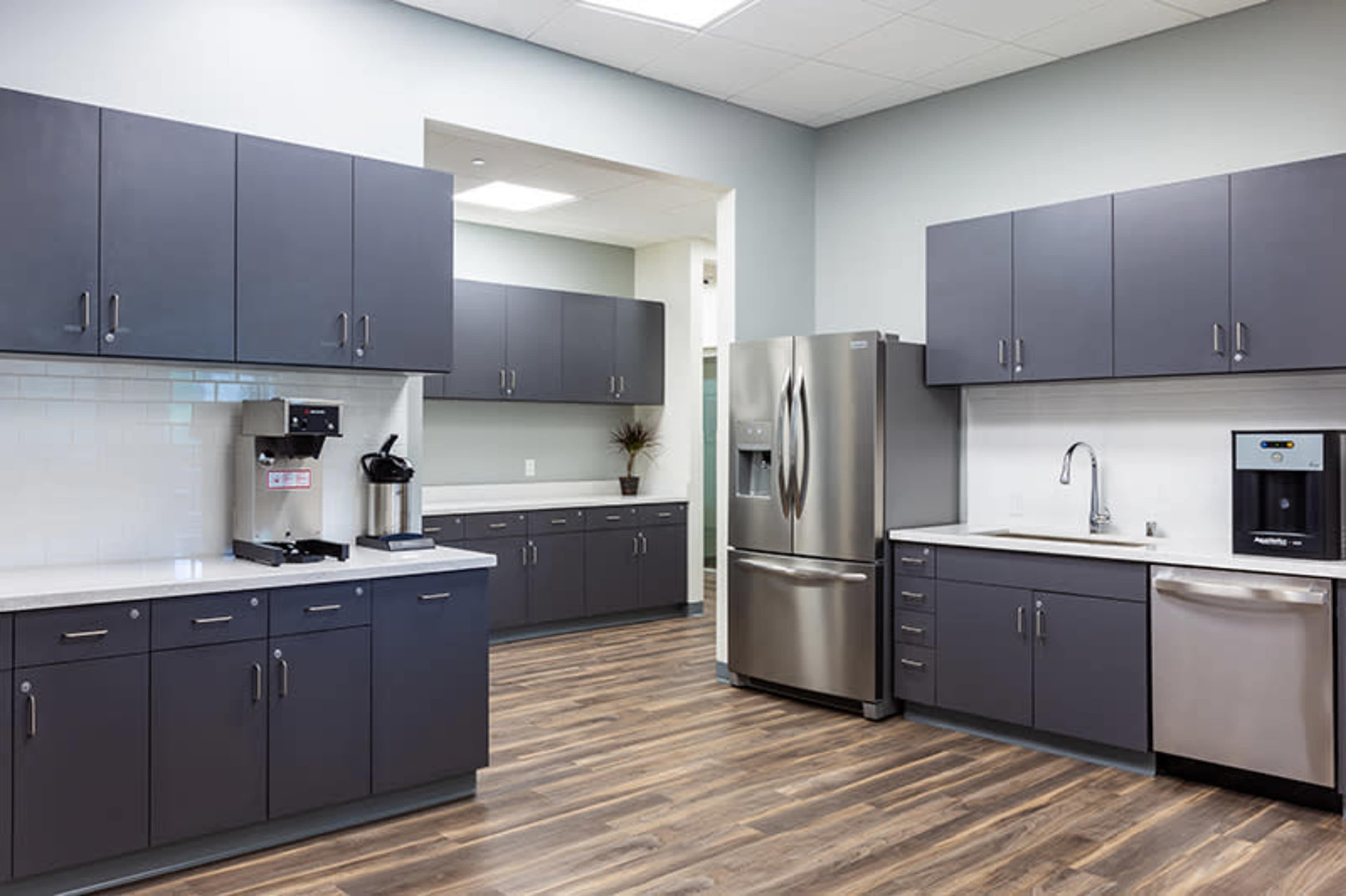 A modern kitchen with gray cabinets, a stainless steel refrigerator, and a coffee station.