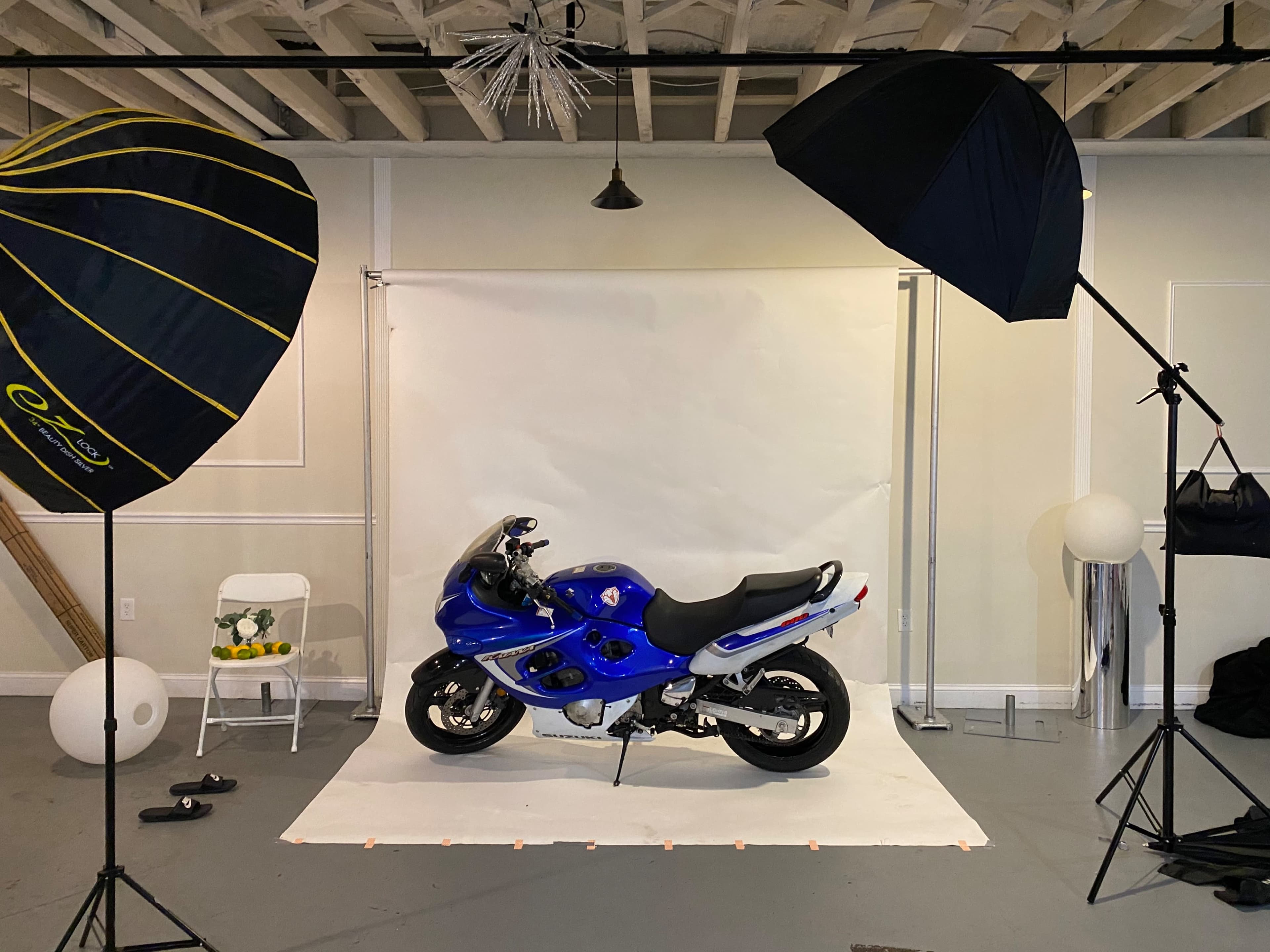 A blue motorcycle is positioned on a white backdrop in a photography studio, flanked by two large softbox lights.