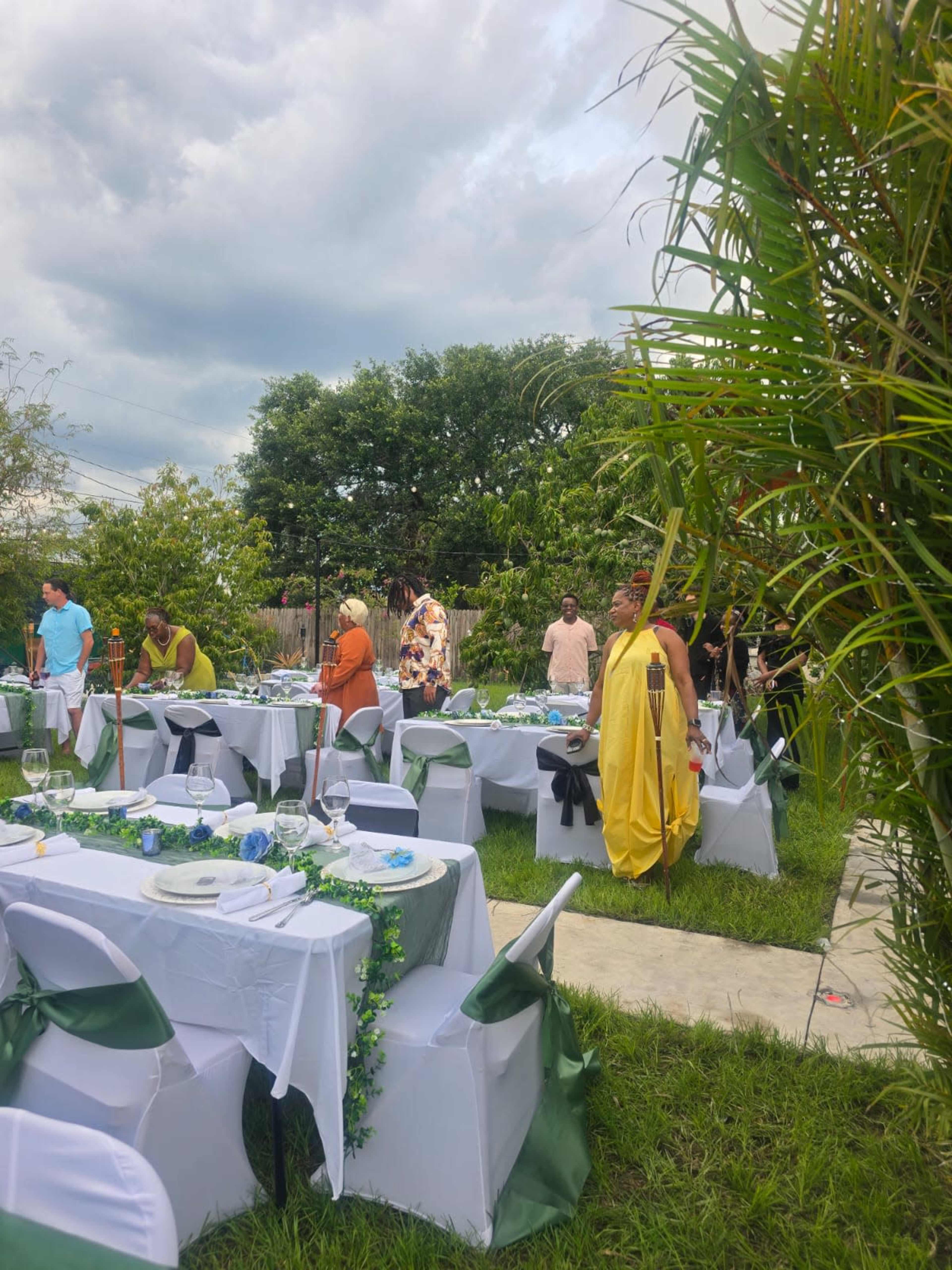 A group of people is gathering in a garden setting prepared with tables and chairs for an outdoor event.