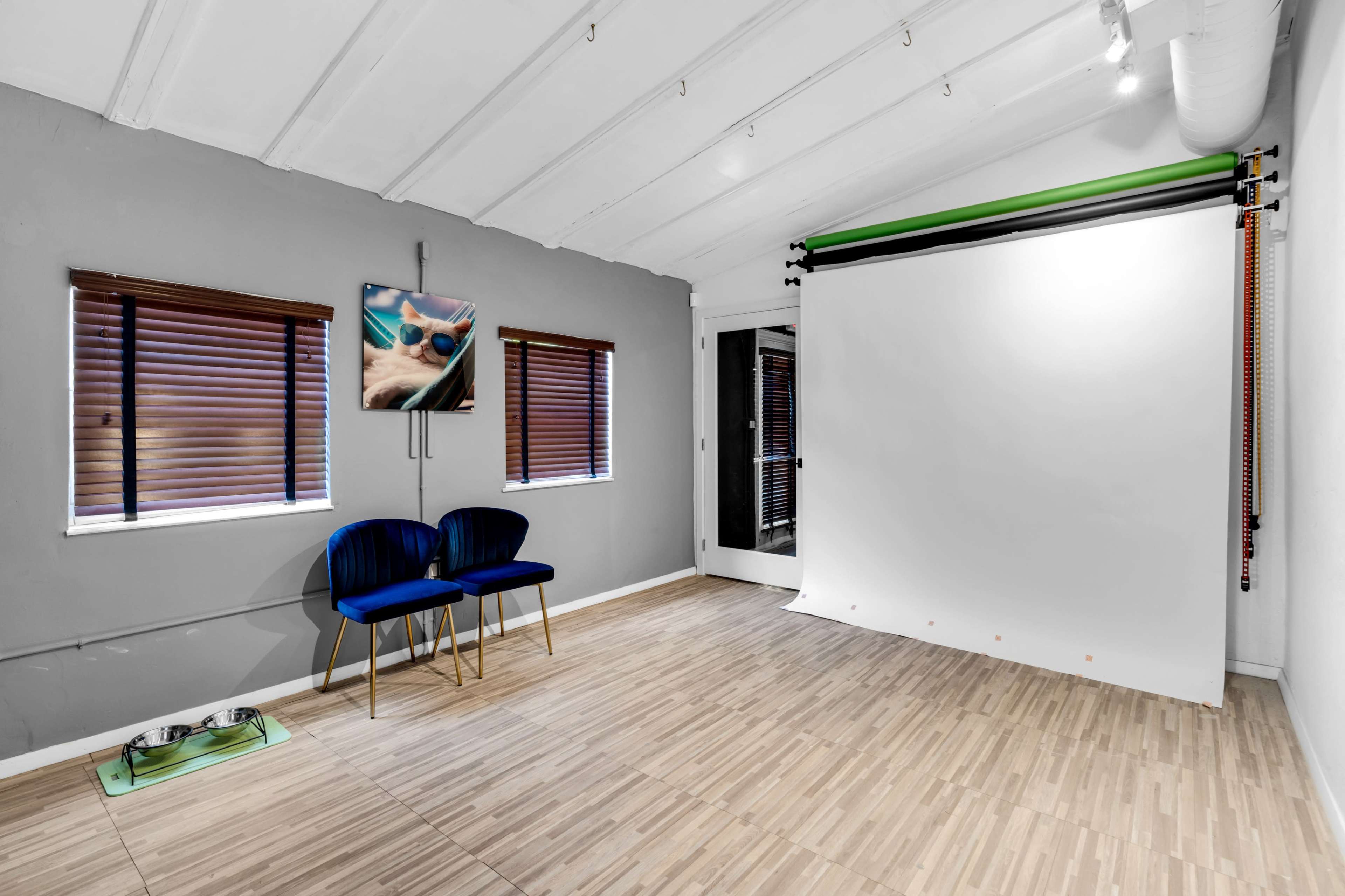 A photography studio with a white backdrop, two blue chairs, and a pet bowl on the floor.