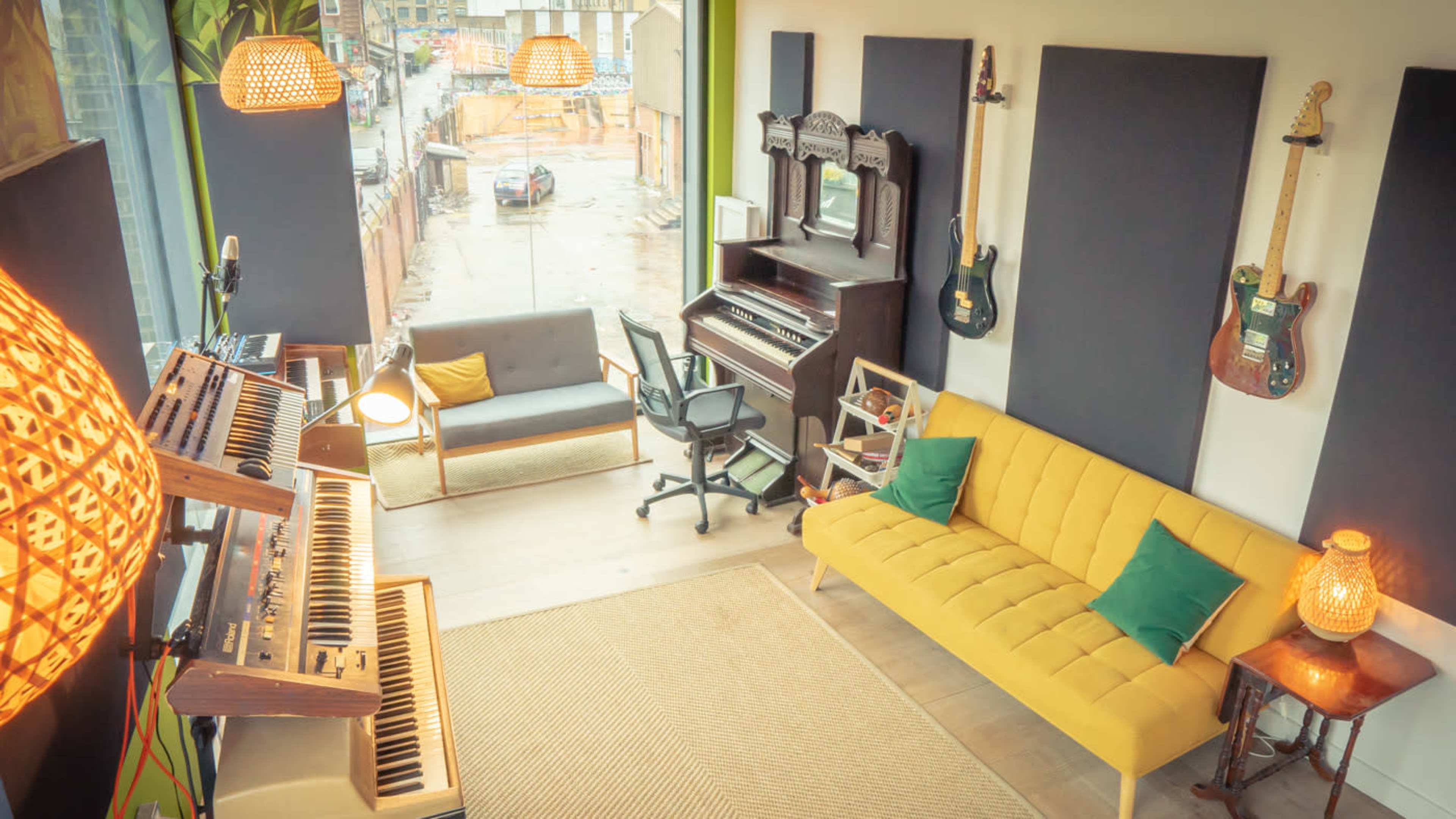 A bright music studio features a yellow sofa, an antique piano, and various musical instruments on display.