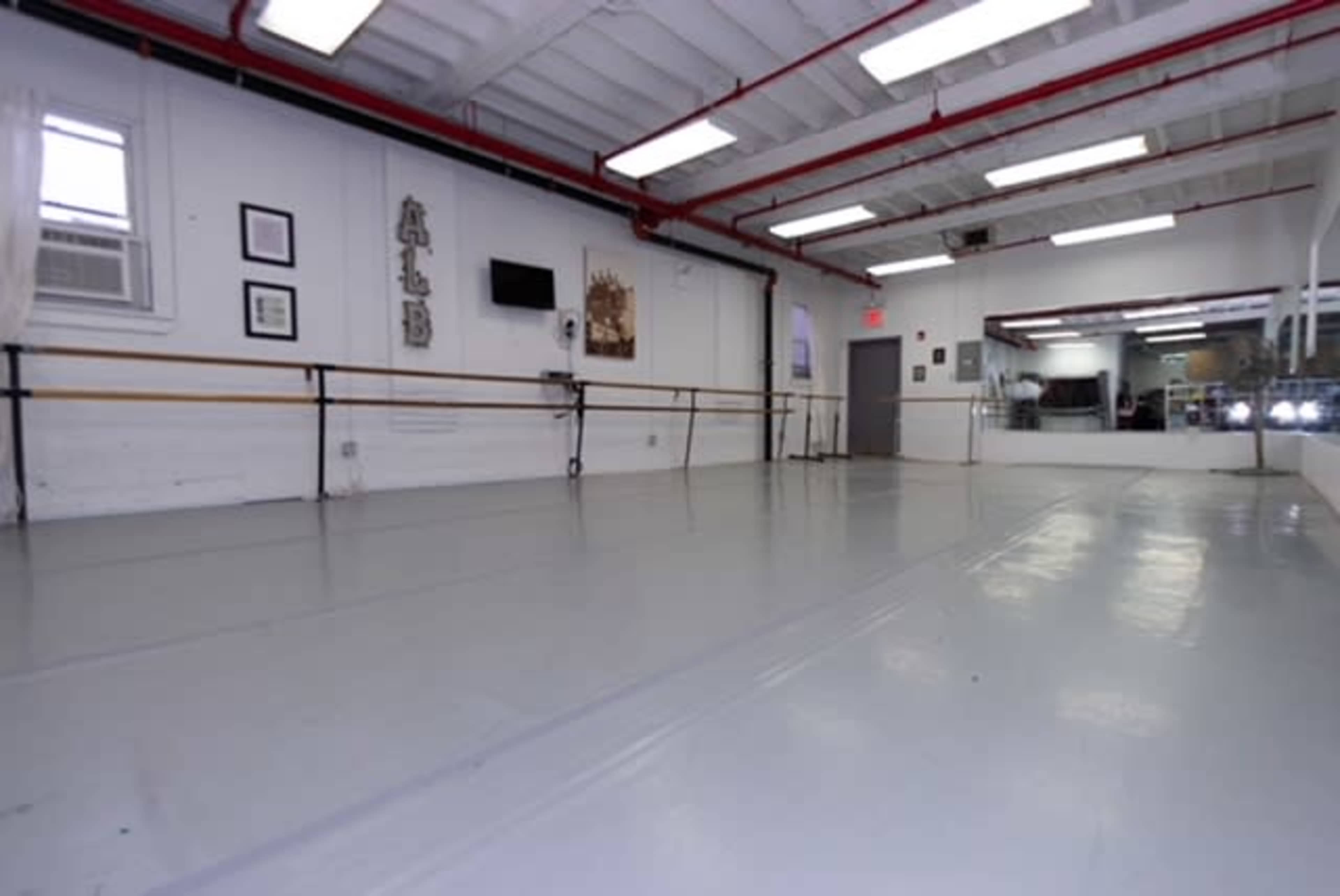 The image shows an empty dance studio with a mirrored wall, wooden ballet barres, and a polished gray floor.