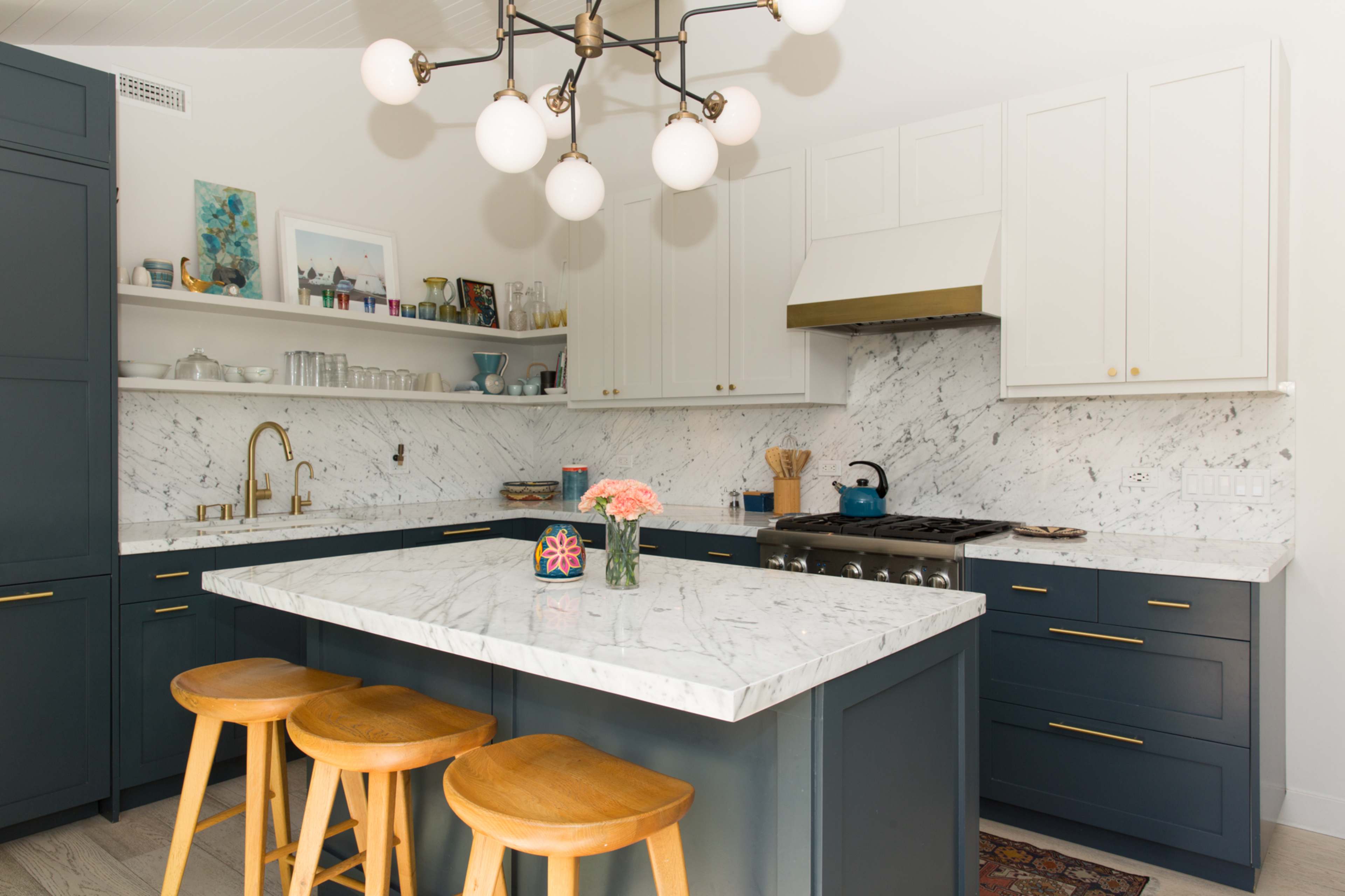 A modern kitchen featuring navy blue cabinetry, a marble countertop, and a central island with wooden stools.