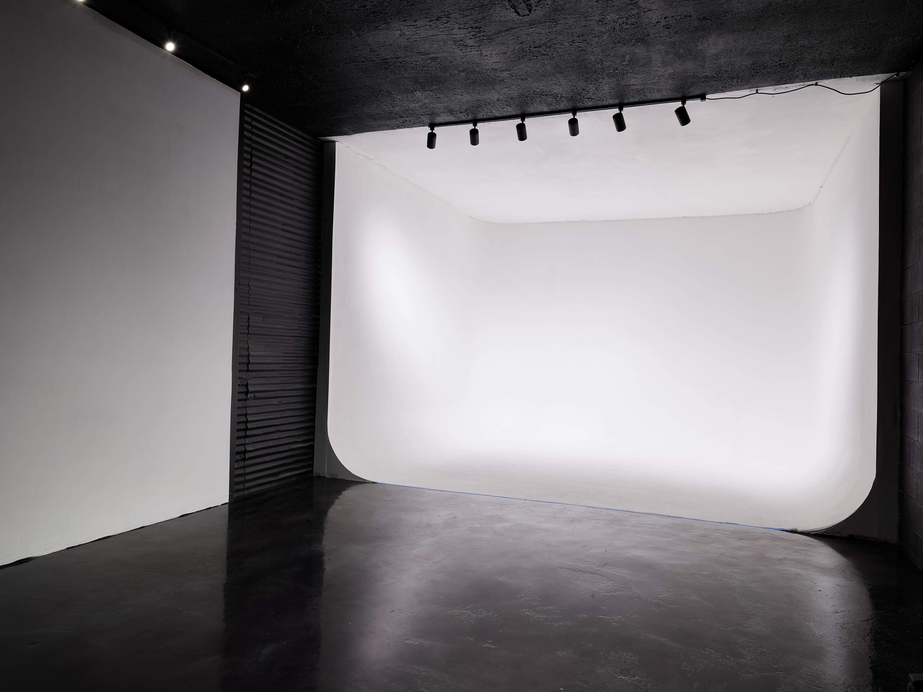 A minimalist photography studio with a curved white backdrop and dark flooring.