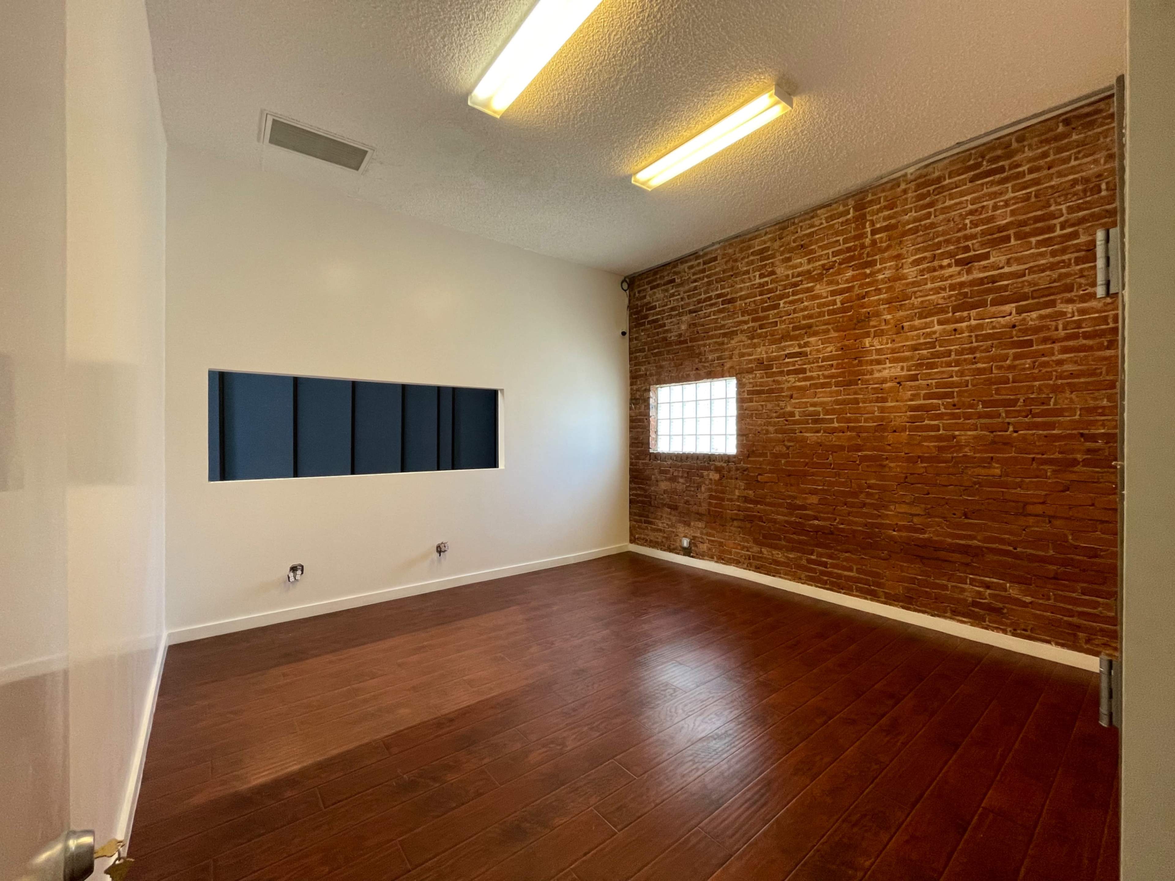 An empty room featuring a brick wall, wooden flooring, and two overhead light fixtures.