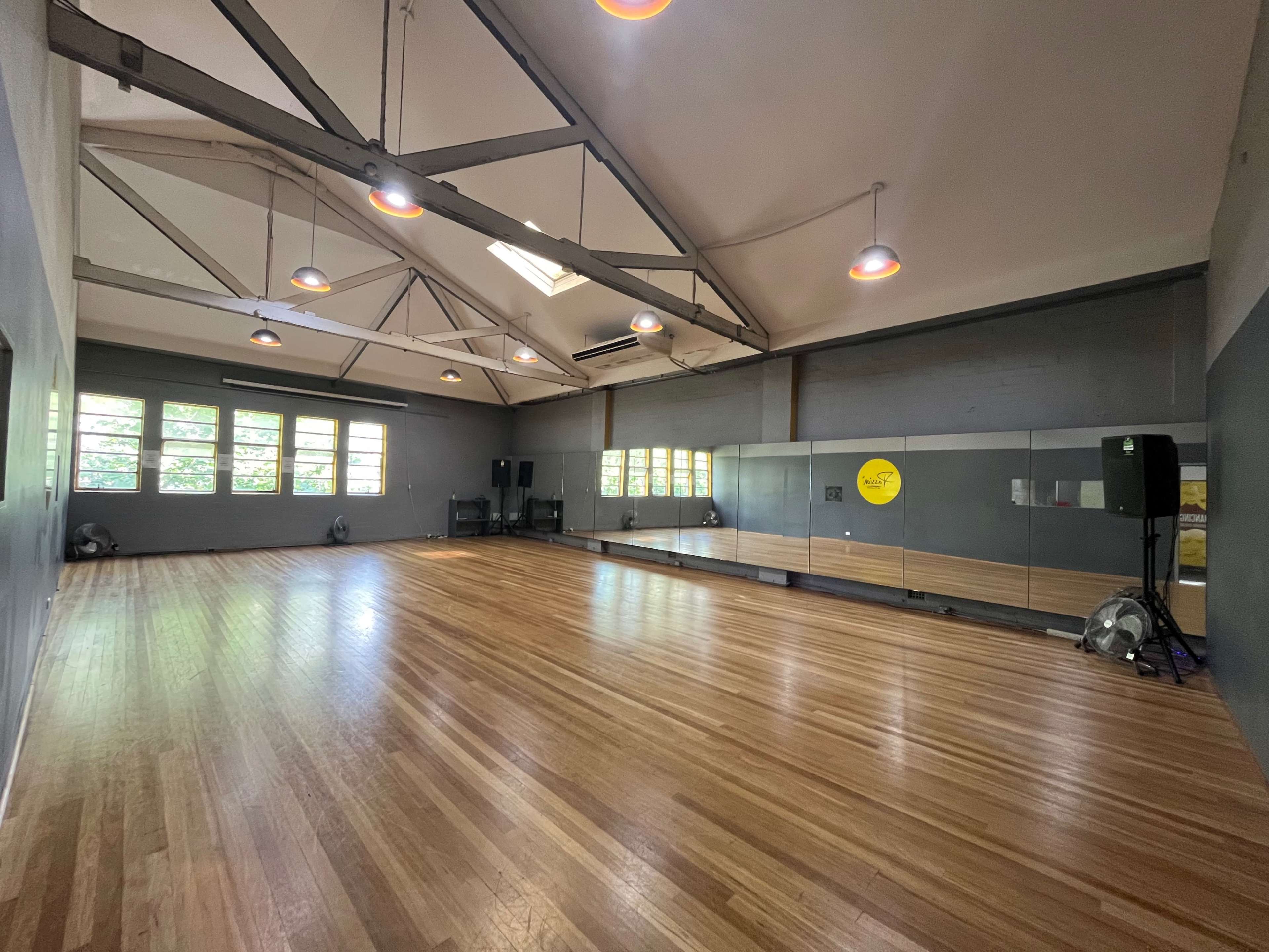 The image shows a spacious dance studio with hardwood floors, large windows, and mirrors along one wall.
