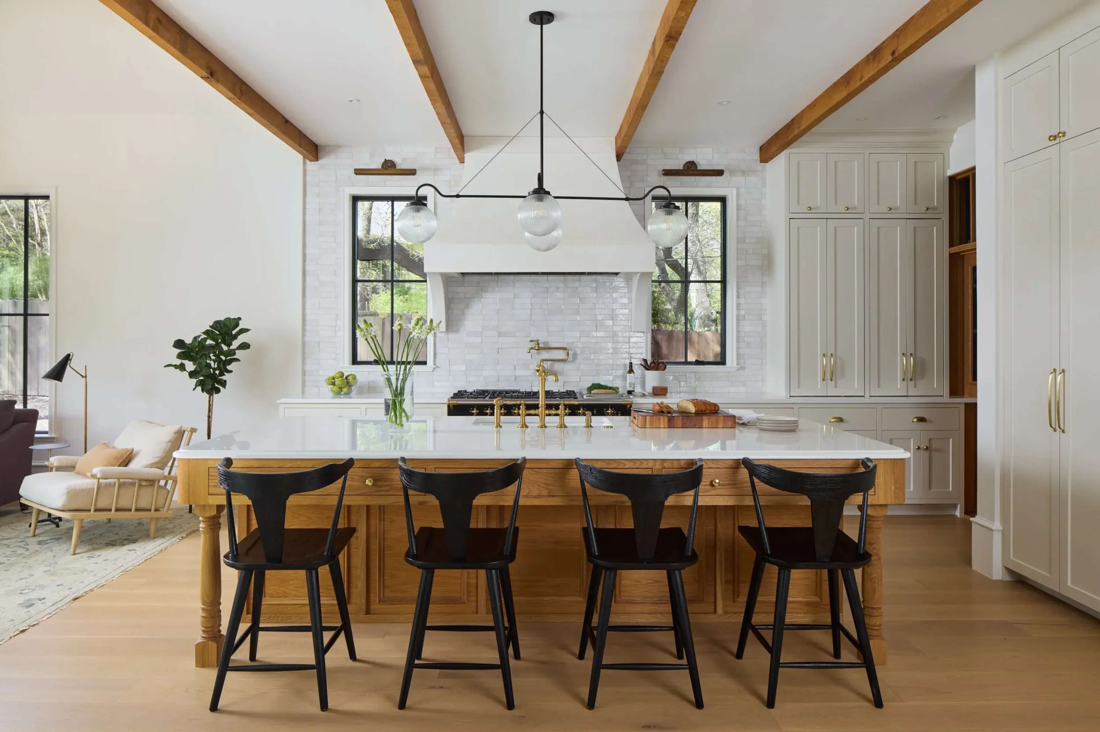 The image shows a modern kitchen with wooden beams, a large island featuring bar stools, and a white brick backsplash behind a stove.