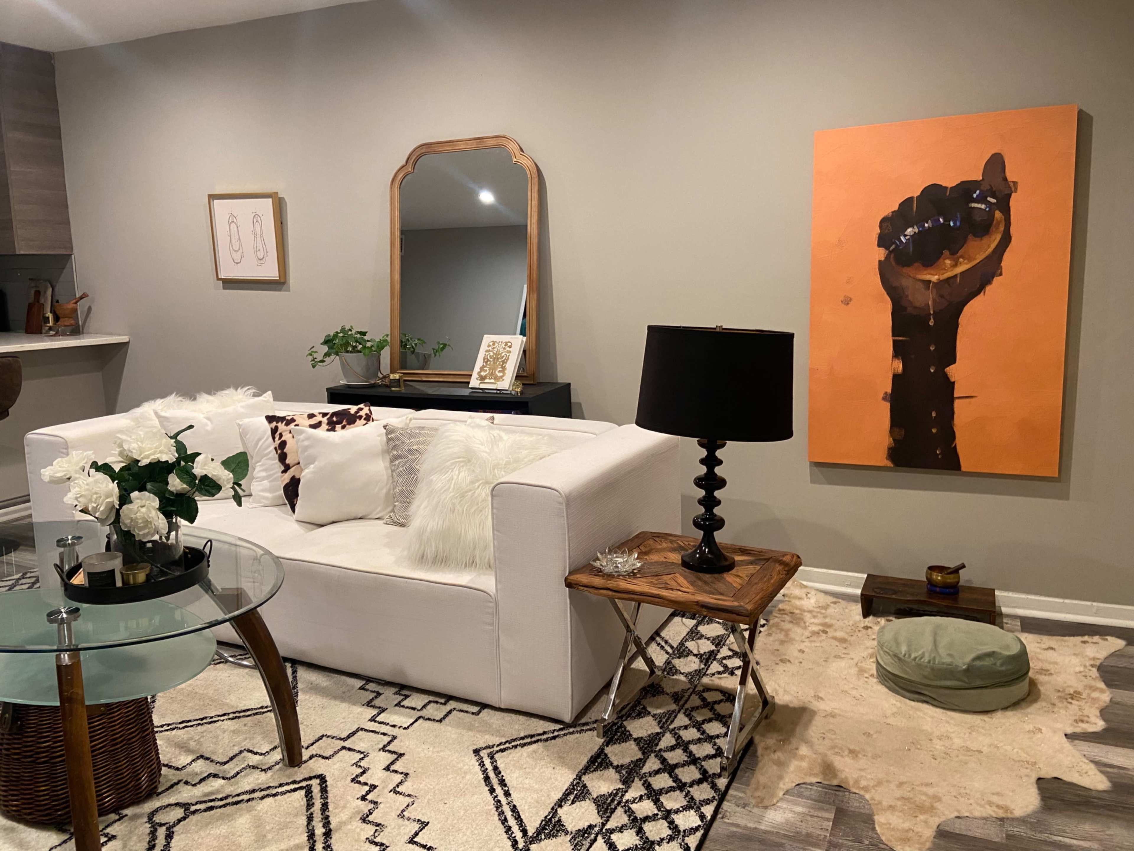 A modern living room with a white sofa, a glass coffee table, and an orange artwork of a raised fist on the wall.