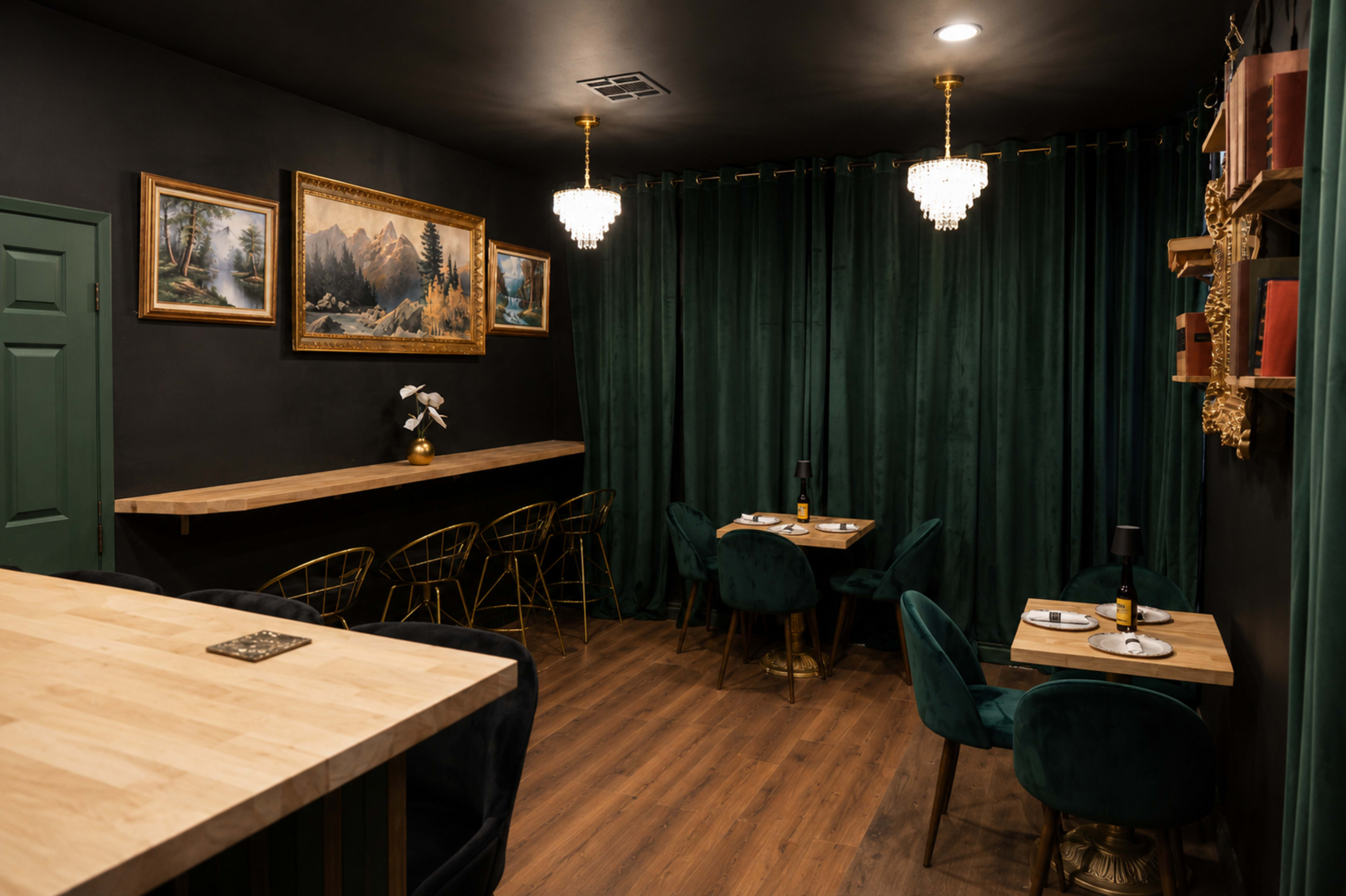 The image shows a cozy dining area with dark green curtains, a wooden bar, and two small tables set with wine glasses.
