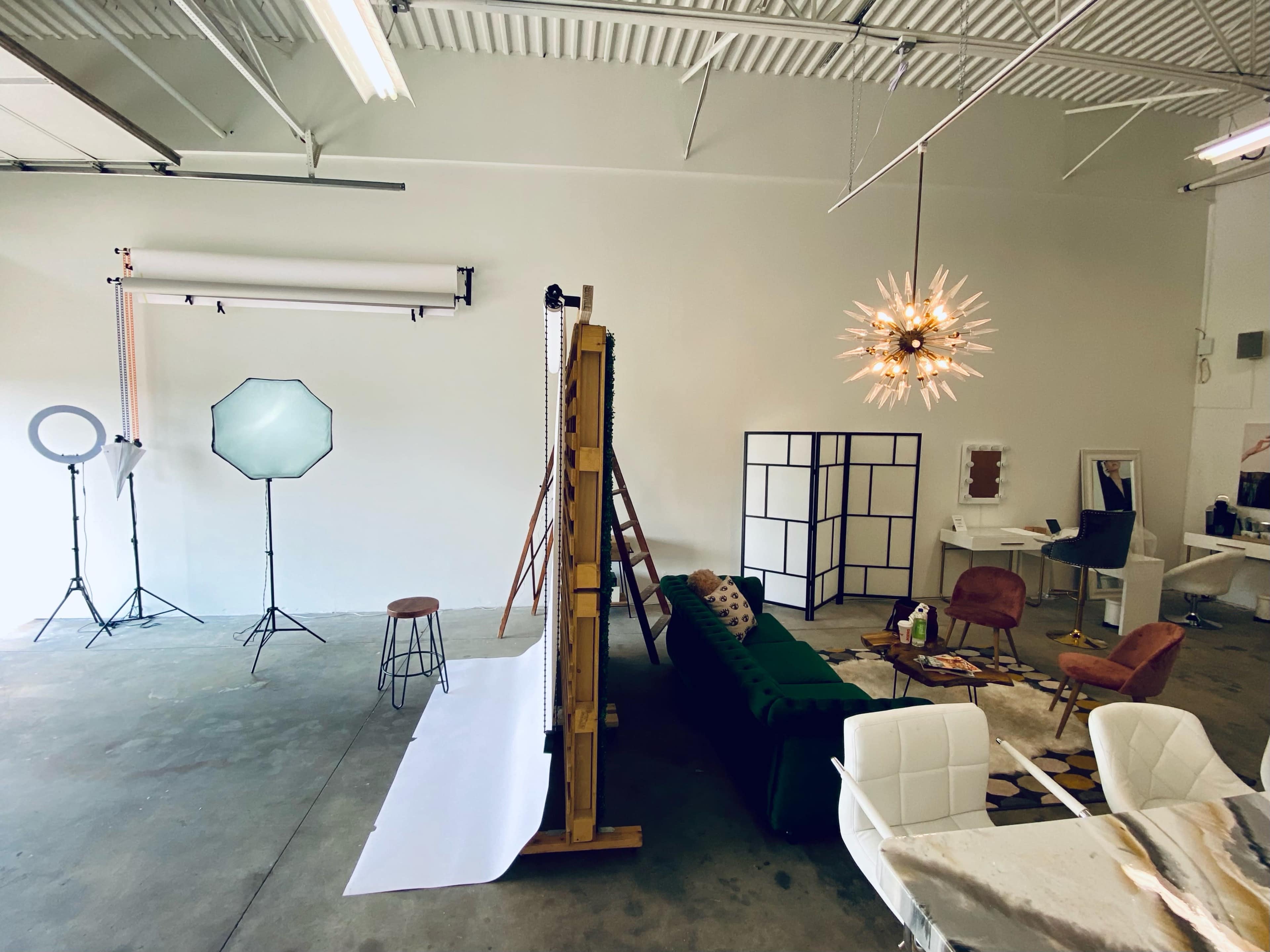 A spacious studio with photography lighting equipment, a green couch, and various props arranged for a photo shoot.