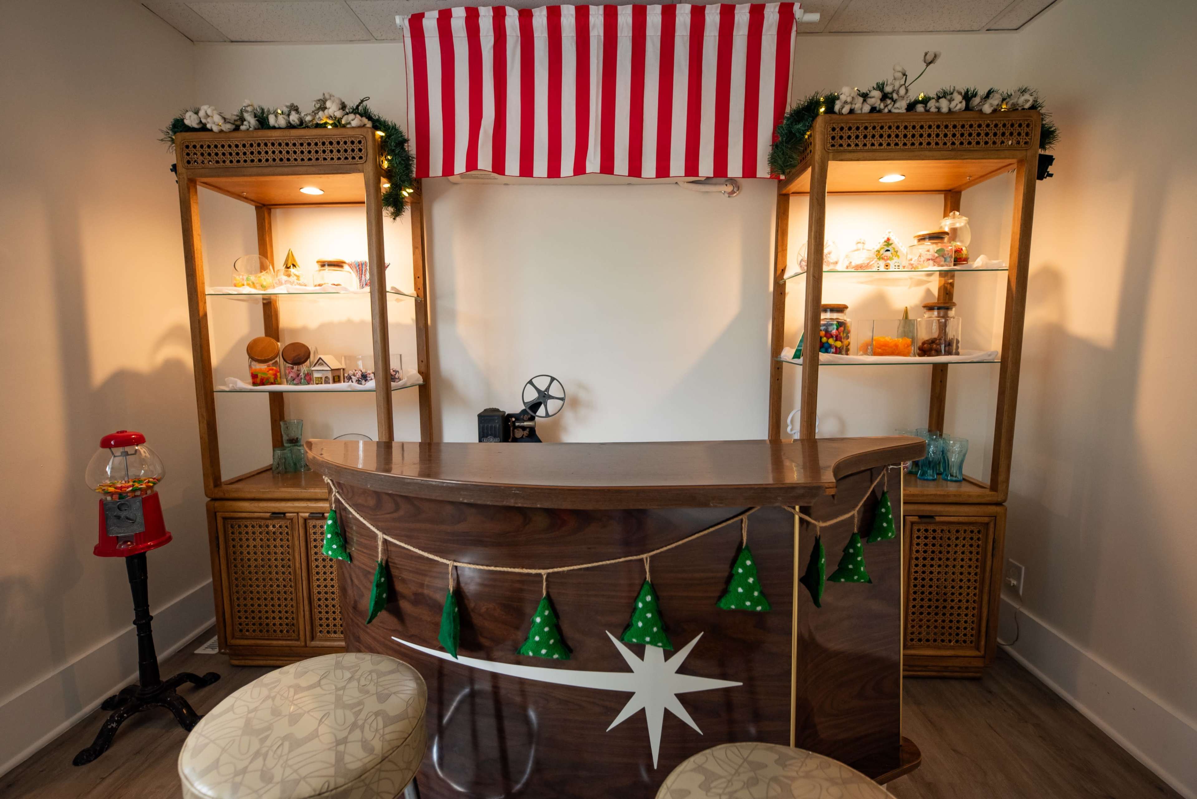 The image shows a cozy snack bar with a wooden counter, striped canopy, decorative green garlands, and shelves displaying various snacks and items.